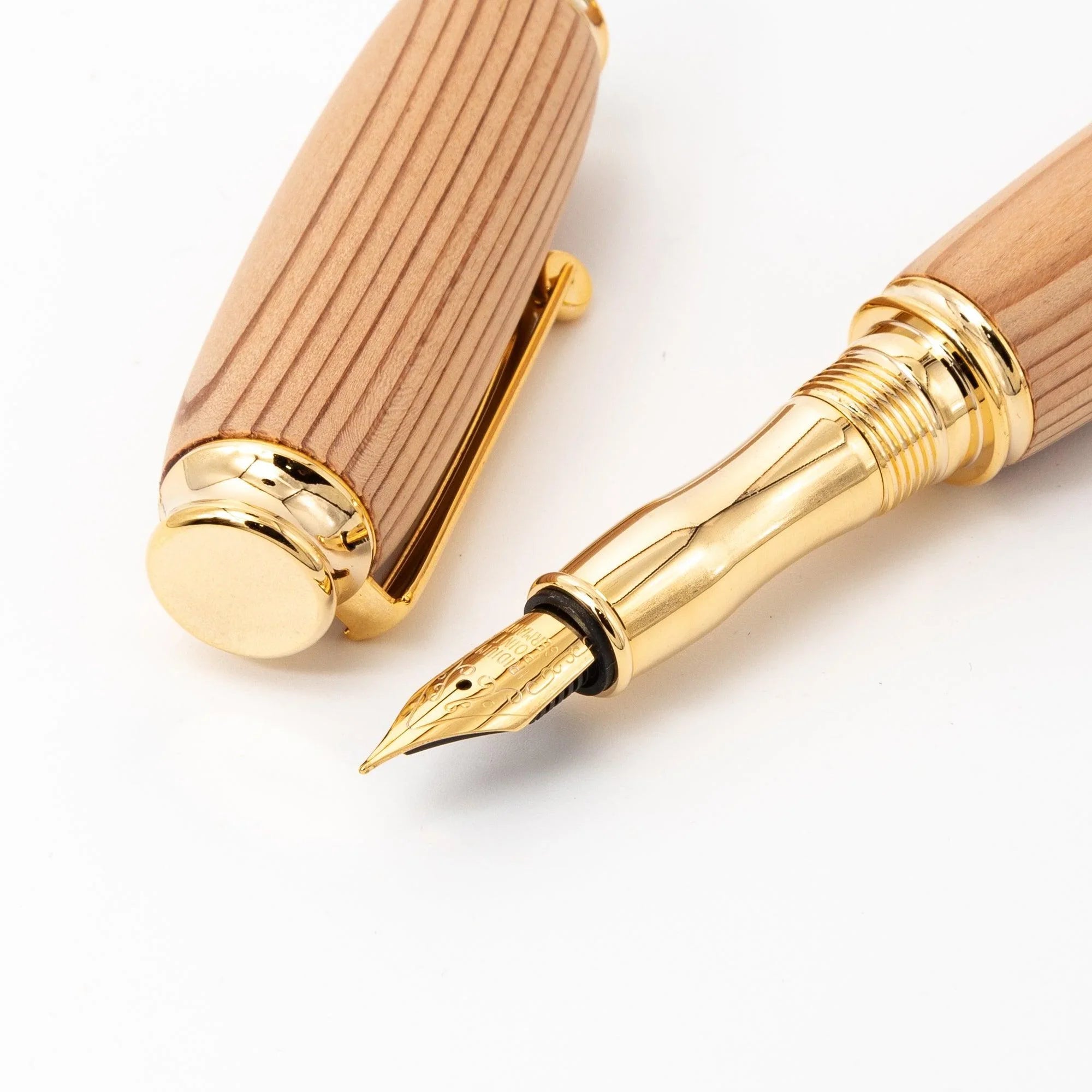 Close-up of cedar wood fountain pen showing gold nib and section beside removed cap, gold trim rings and flat end cap visible