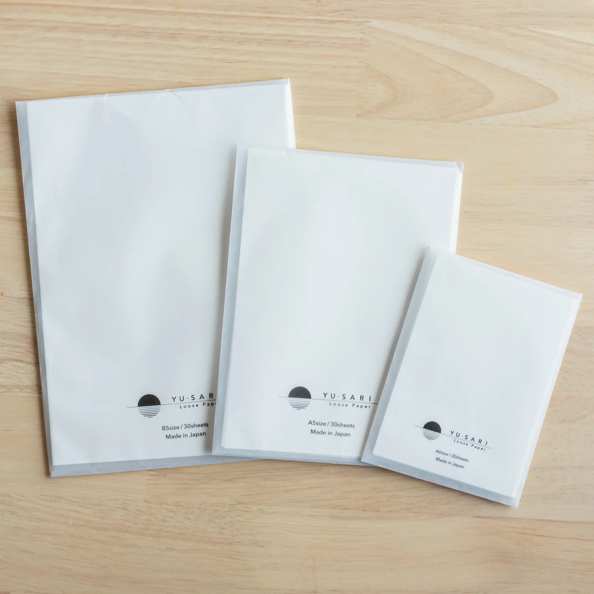 YU-SARI fountain pen loose leaf paper three Japanese-made sizes display on natural wood showing B5 A5 and A4 format stacked