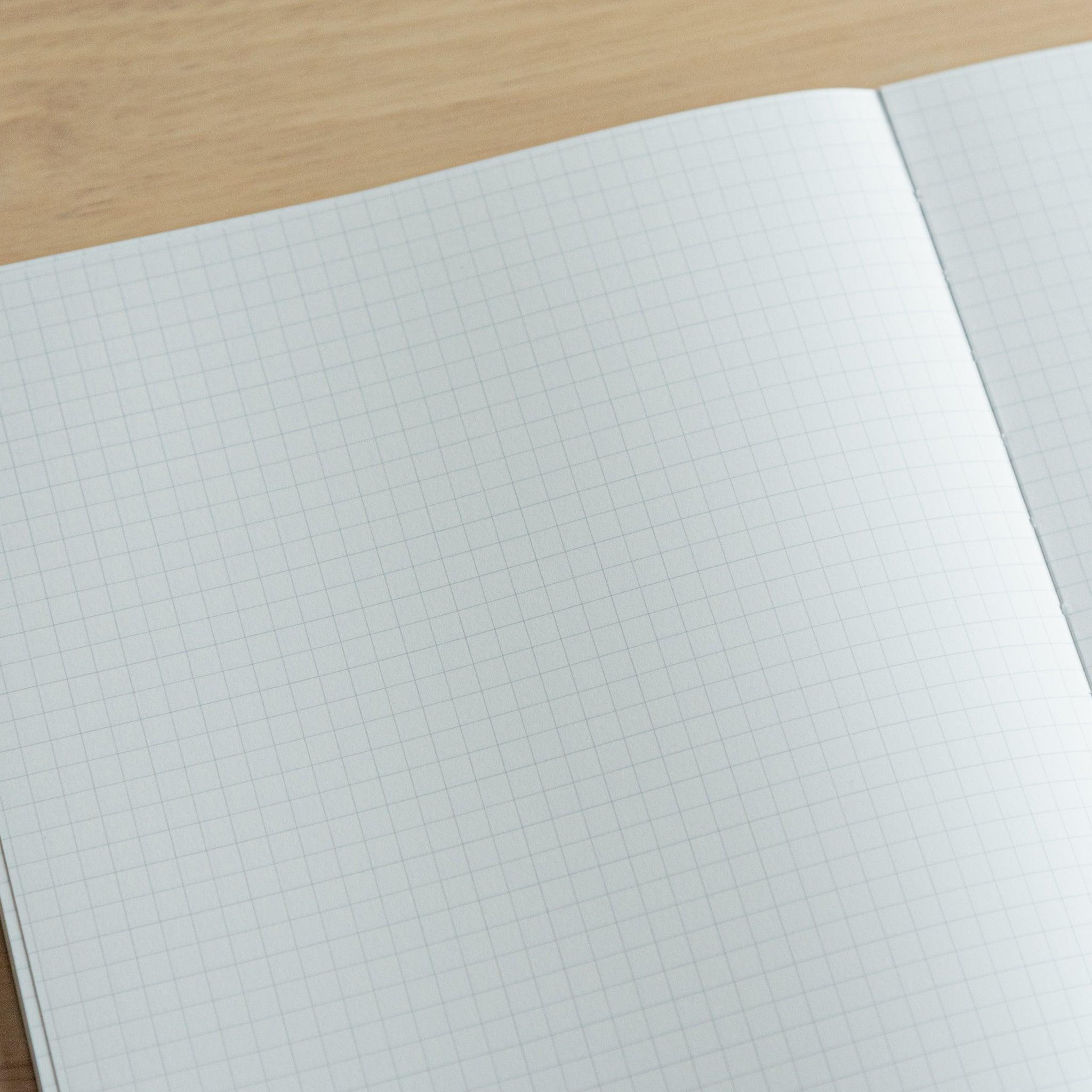 Grid-patterned notebook interior with faint blue lines on white pages, open on a wooden table.