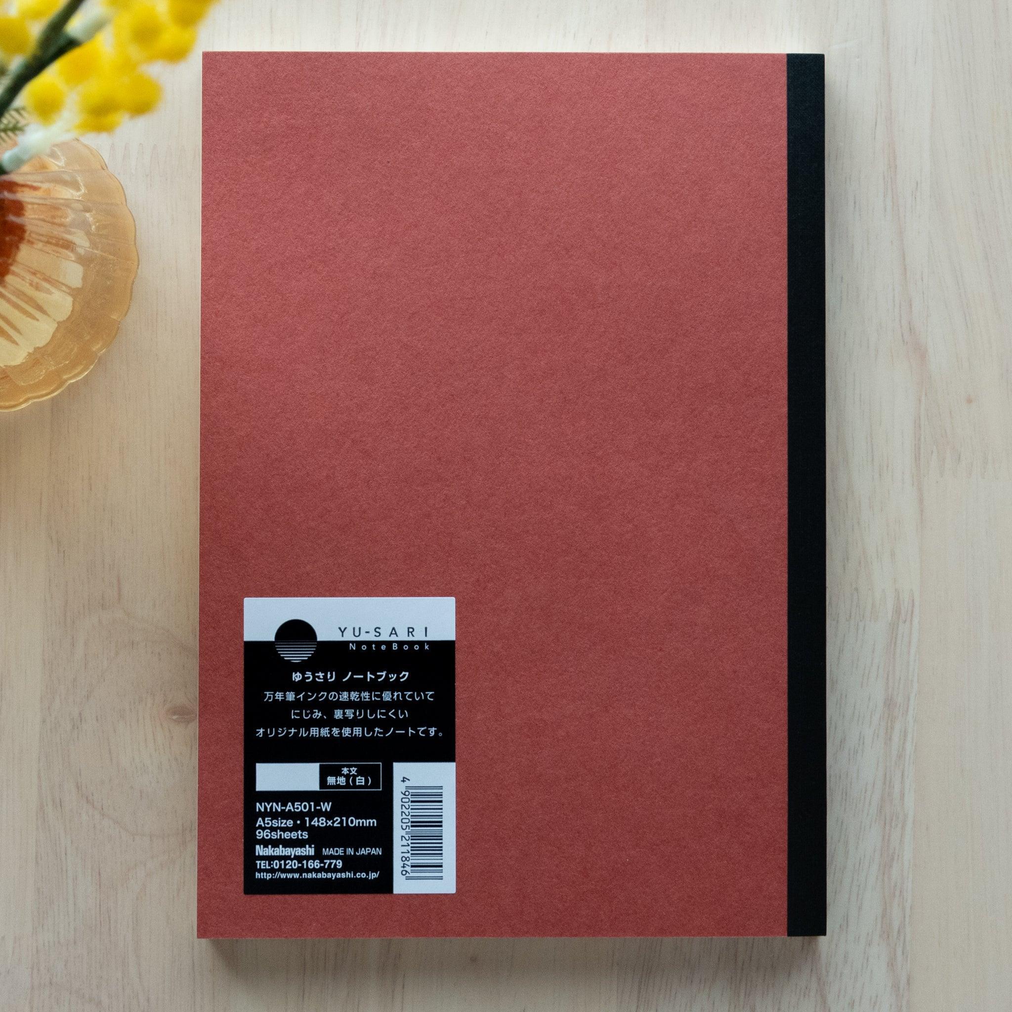 The back cover of a red YU-SARI notebook with a black label providing product details, emphasizing its Japanese origin and fountain pen-friendly paper.