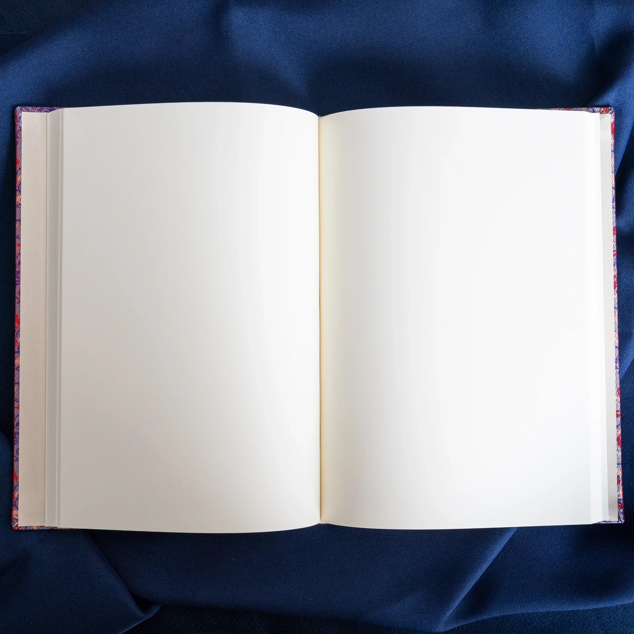Yusoku Hanabishi Nishijin silk notebook open to blank white spread, silk binding edges visible, center spine, blue fabric