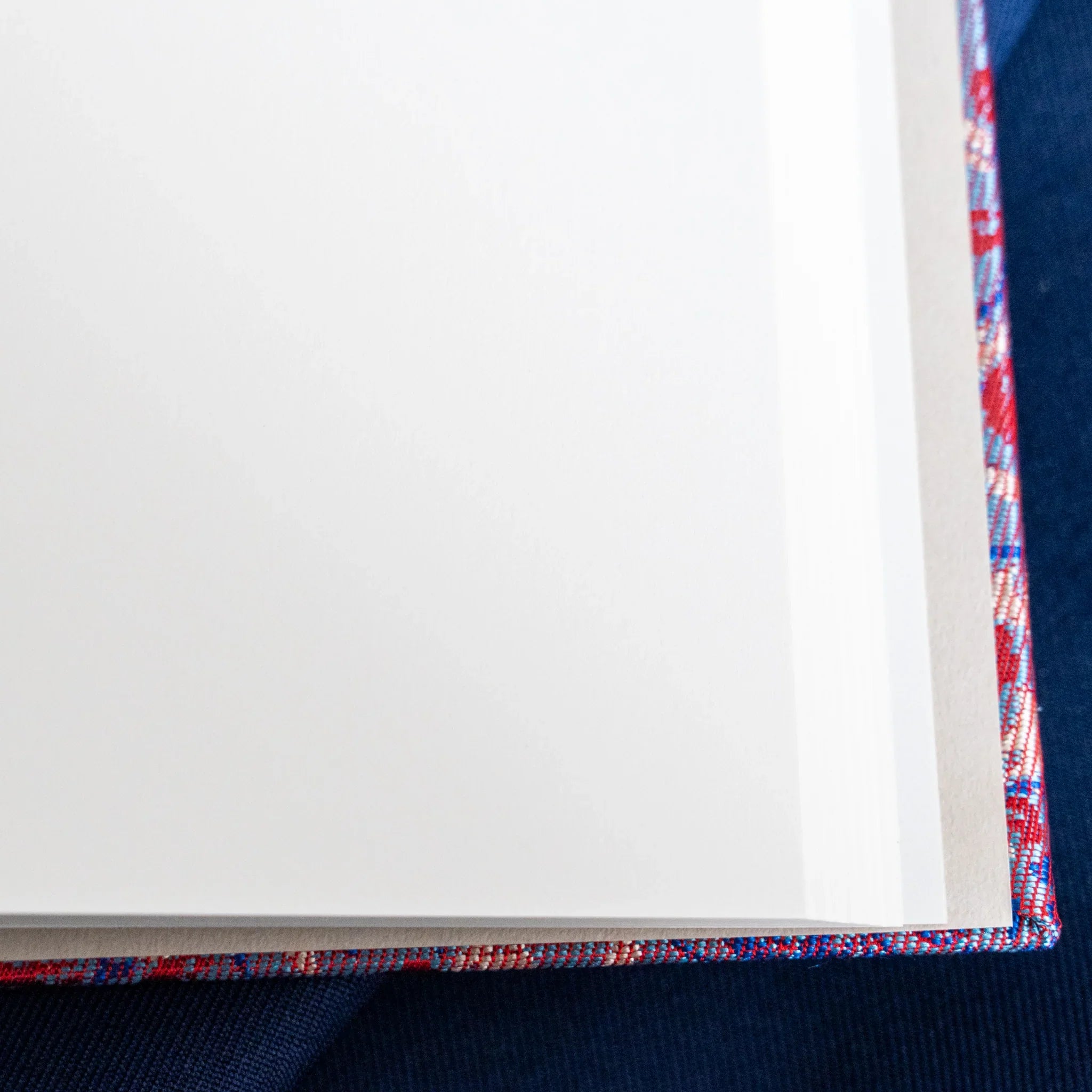 Close-up of open Yusoku Hanabishi Nishijin silk notebook corner, white pages and colorful silk spine binding visible
