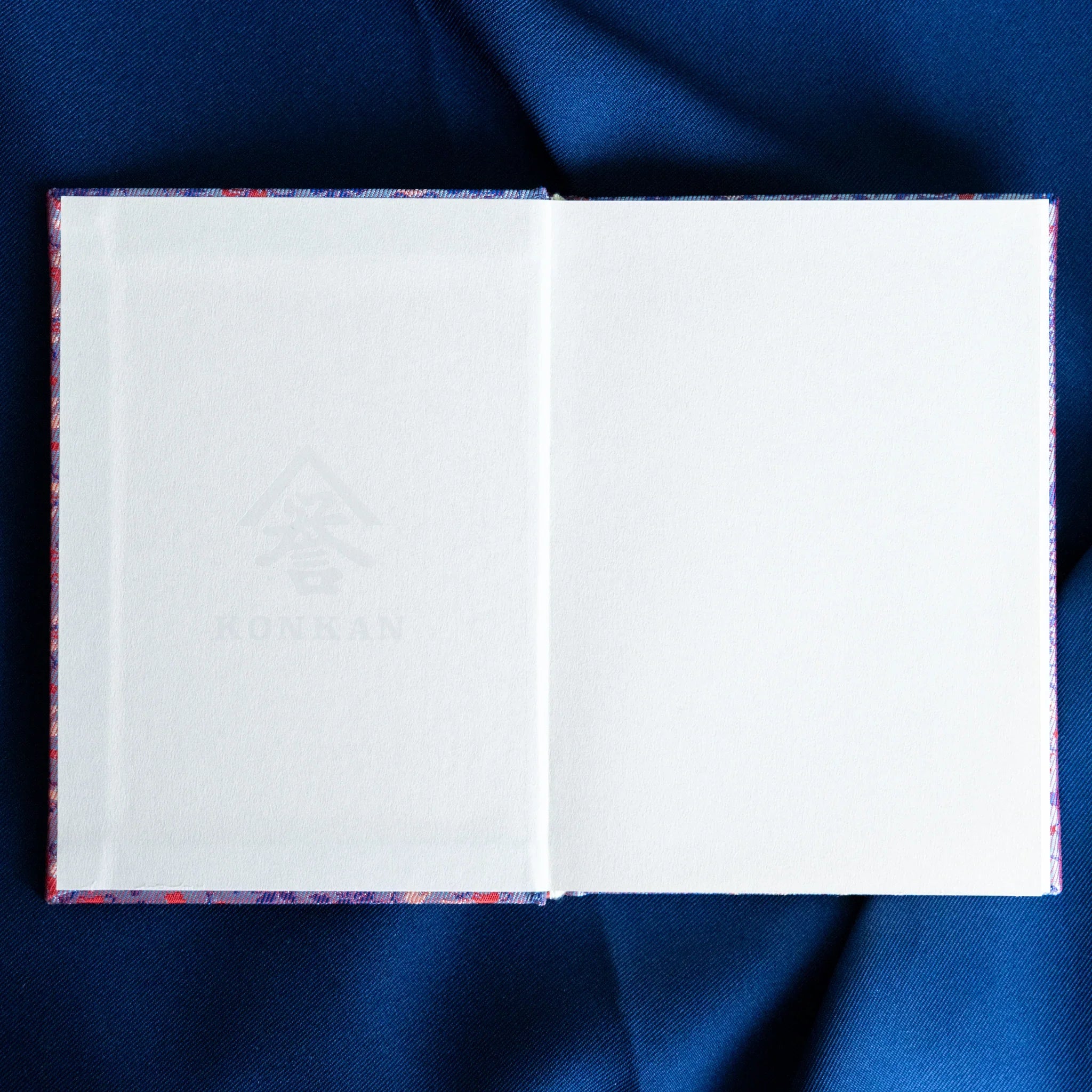 Yusoku Hanabishi Nishijin silk Homeicho notebook open flat showing two blank white pages with lavender-pink cover spine