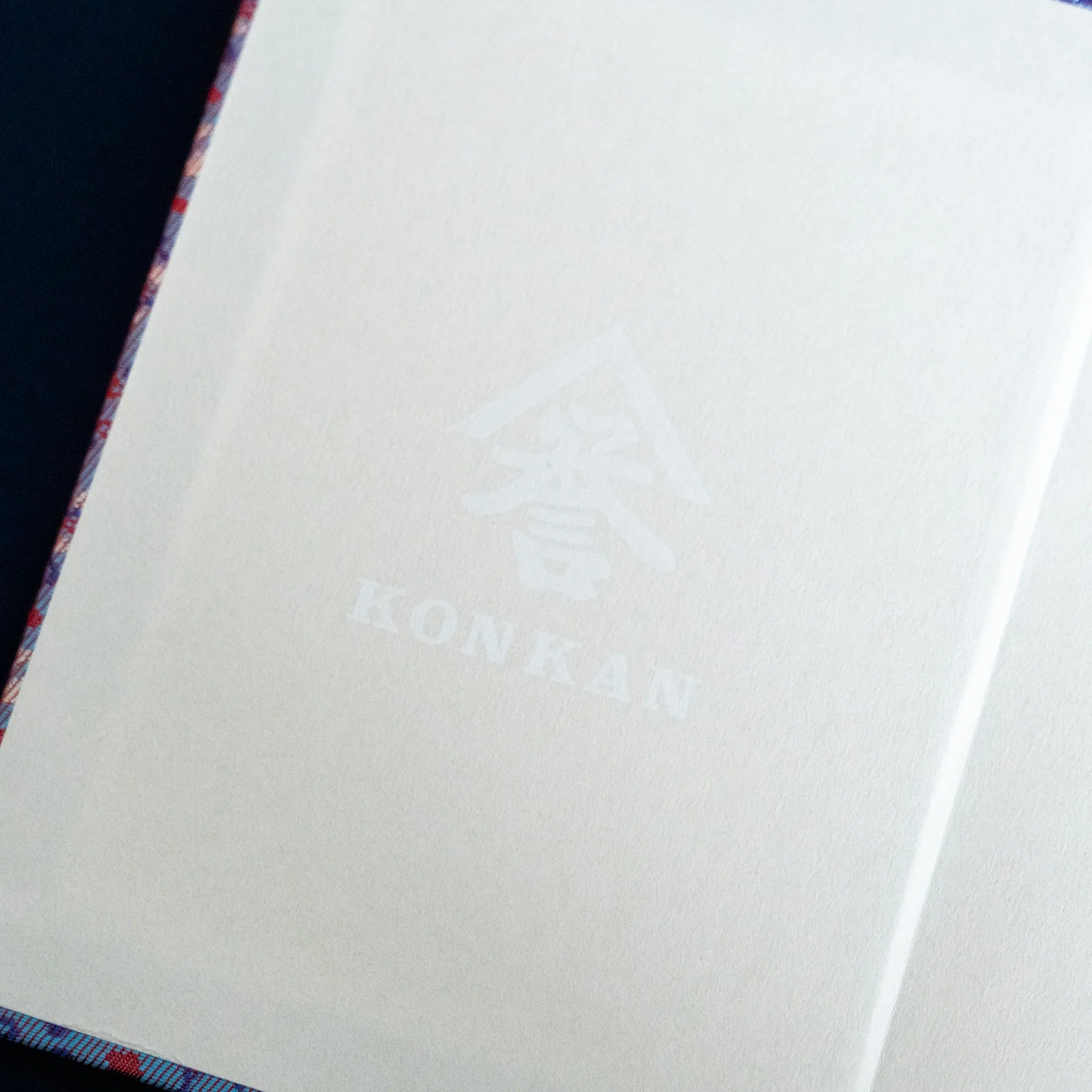 Yusoku Hanabishi Nishijin silk notebook interior page with Komorebi watermark and lavender-pink silk cover edge visible
