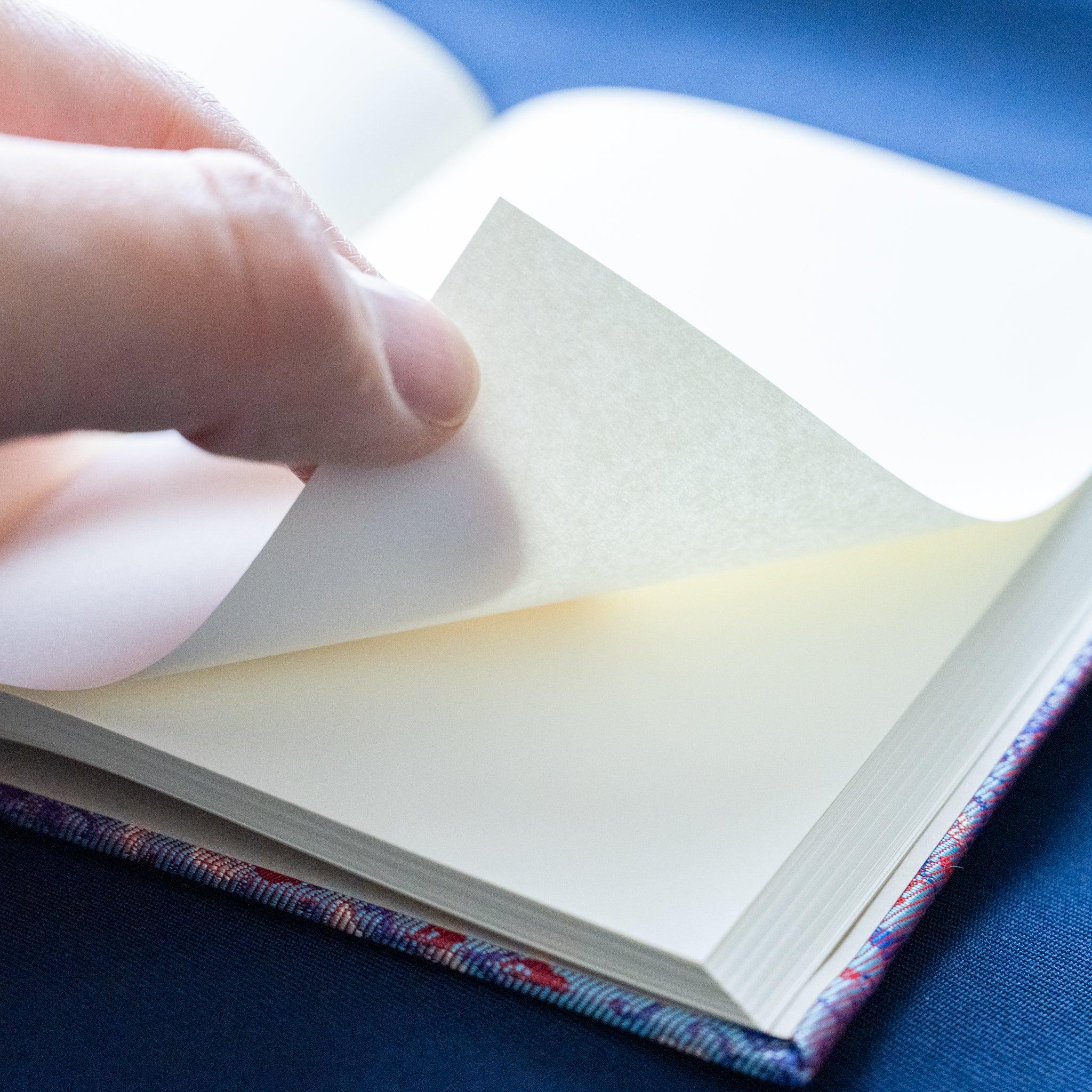 Hand turning pages of Yusoku Hanabishi Nishijin silk Homeicho notebook with lavender-pink woven cover visible at base