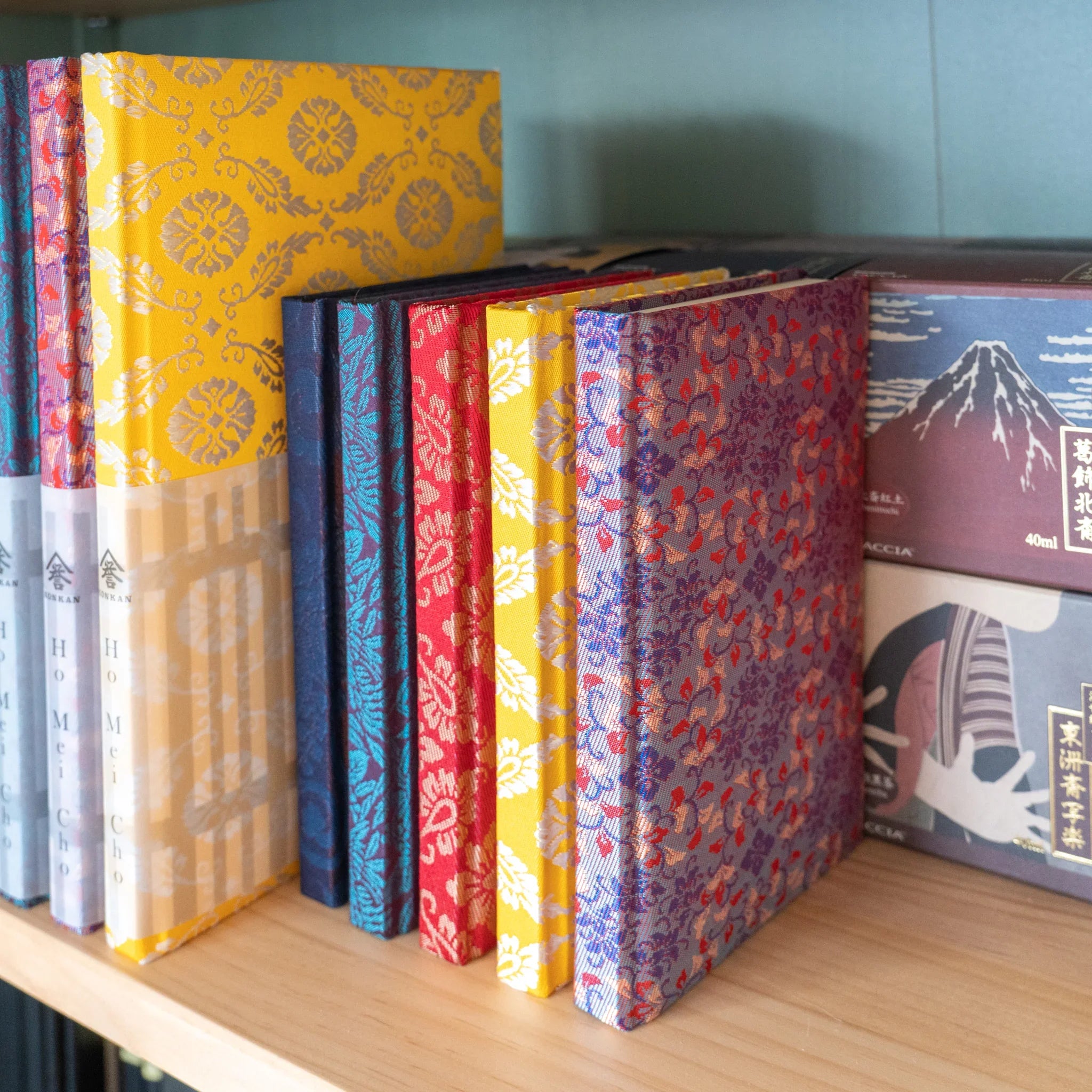 Collection of Yusoku Hanabishi Nishijin silk Homeicho notebooks in multiple colors standing on wooden shelf
