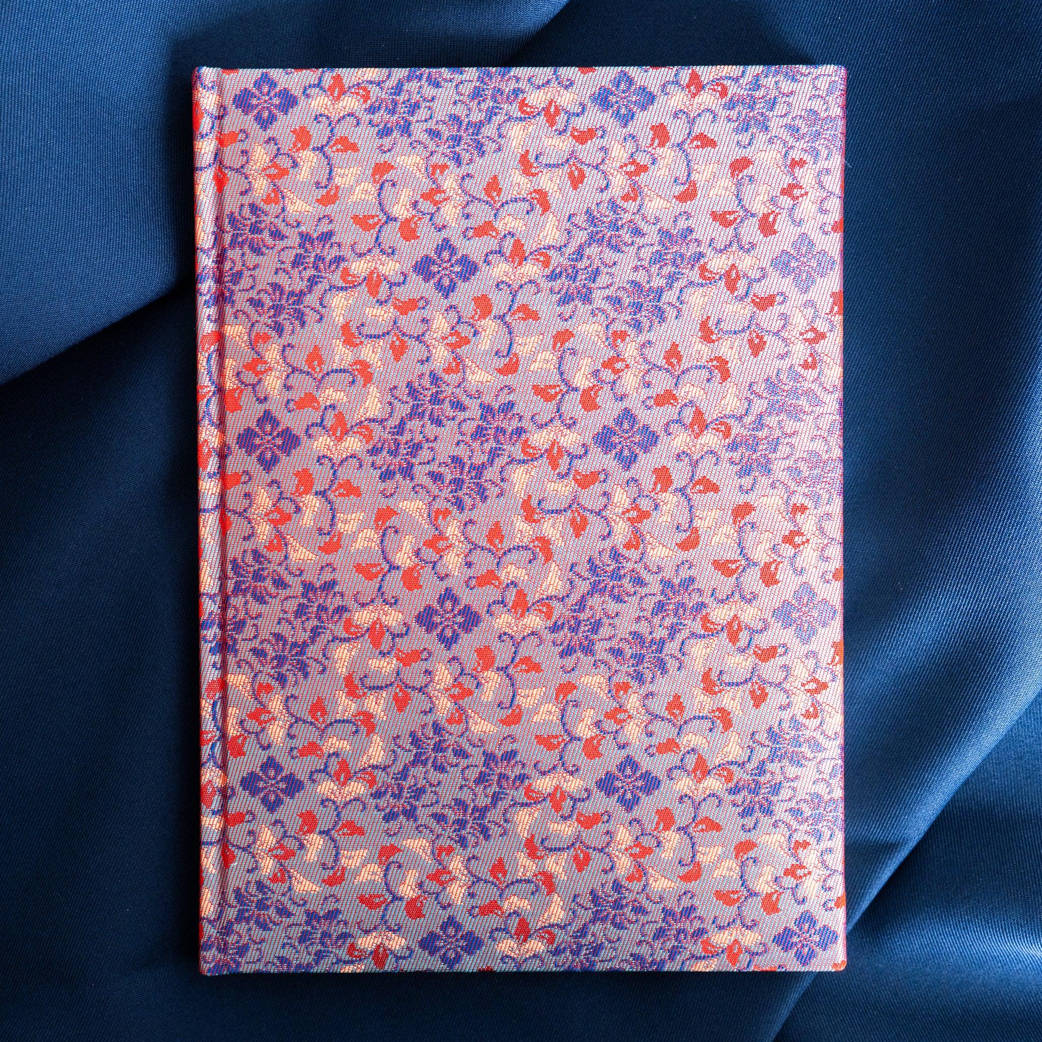 Yusoku Hanabishi Nishijin silk notebook front cover, full blue and red woven floral pattern, no belly band, on blue fabric