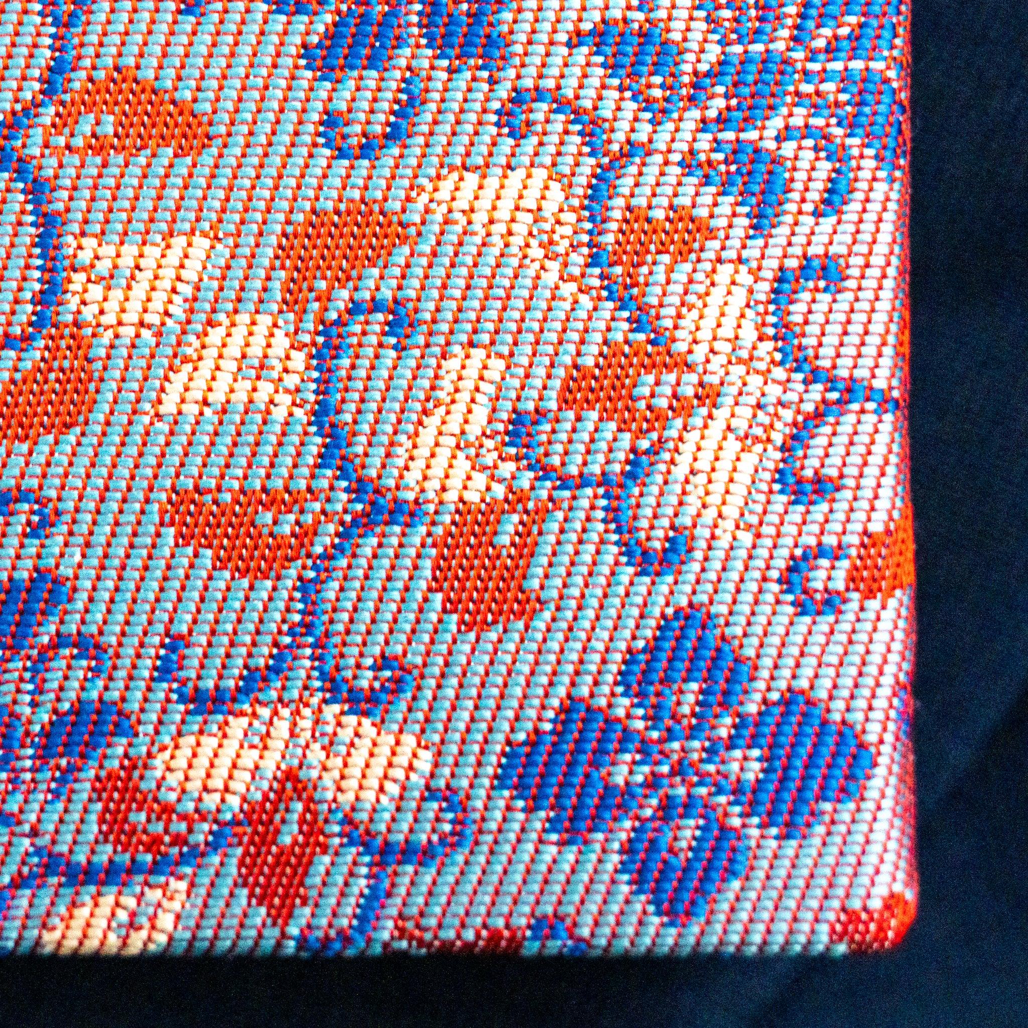 Close-up of Nishijin silk weave texture showing red and orange floral pattern on blue ground, individual threads visible