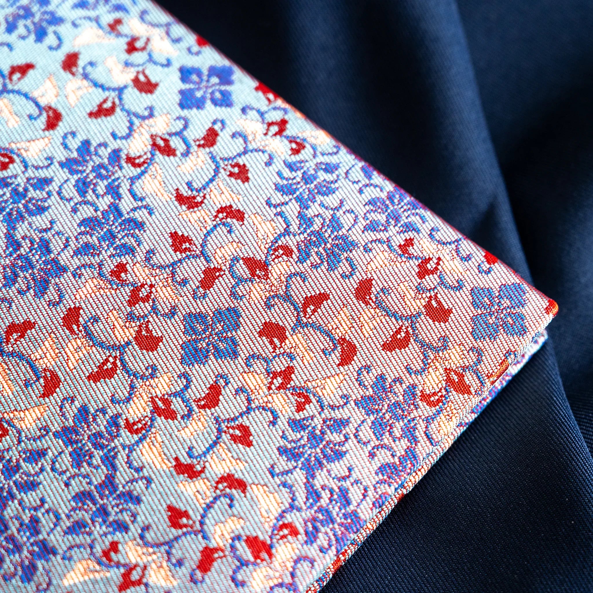 Yusoku Hanabishi Nishijin silk notebook cover corner detail, blue base with red floral woven motifs, on dark blue fabric