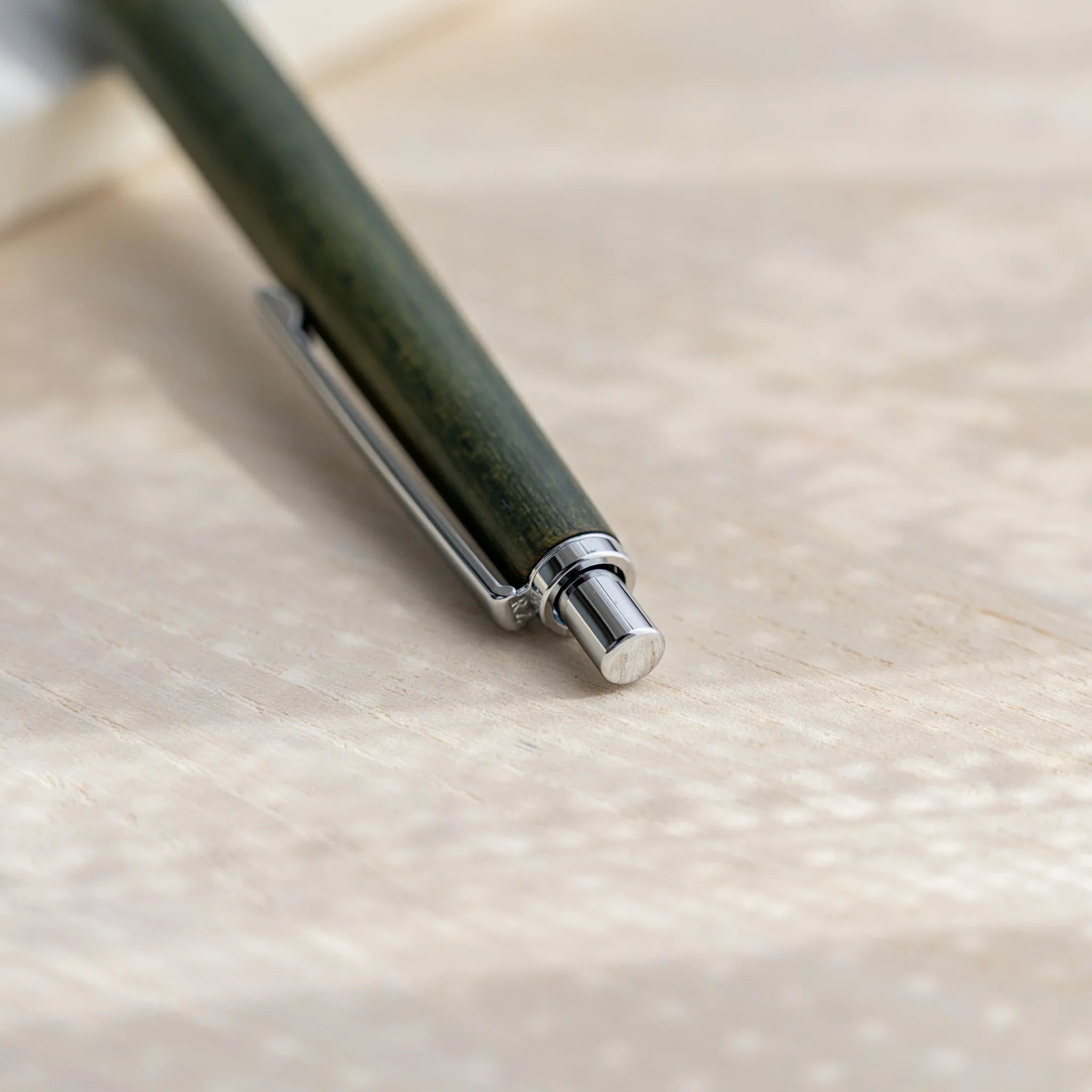 Olive green zelkova wood urushi mechanical pencil, close-up of mid barrel grain and silver clip, Japanese keyaki