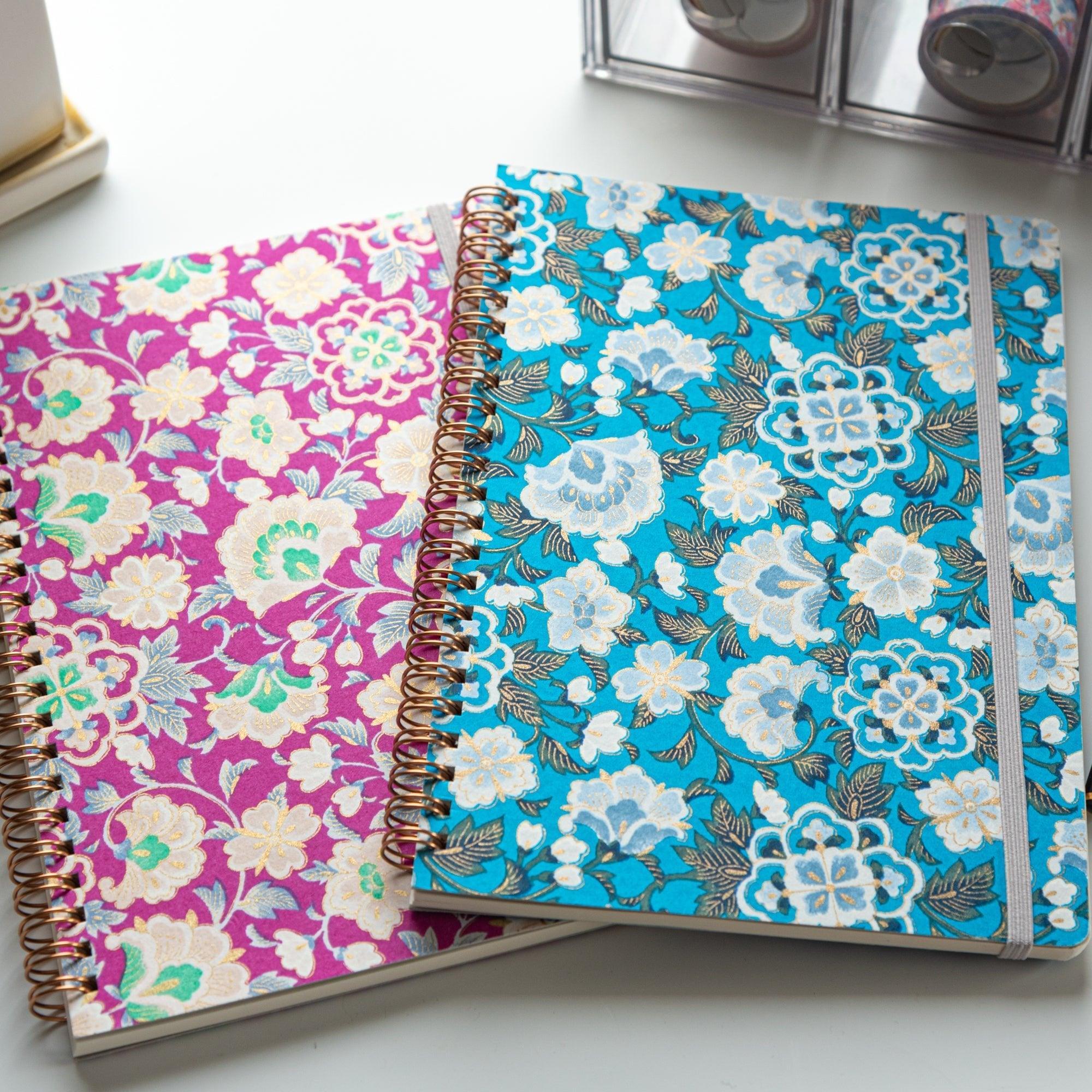 Two Japanese notebooks with Yuzen washi covers. One features a pink floral design, the other blue, both with rose gold spiral bindings.