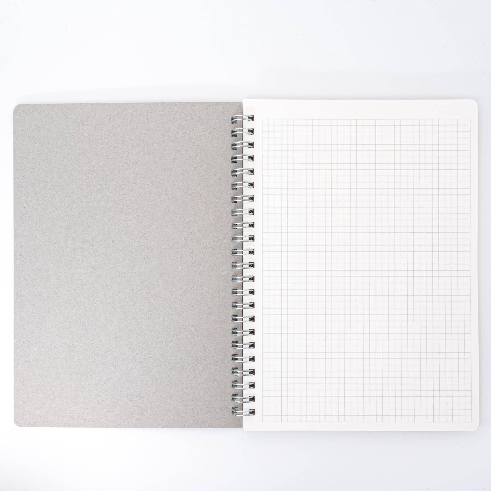 Open spiral-bound notebook with grid paper and a plain cardboard back cover, emphasizing functionality and simplicity in design.