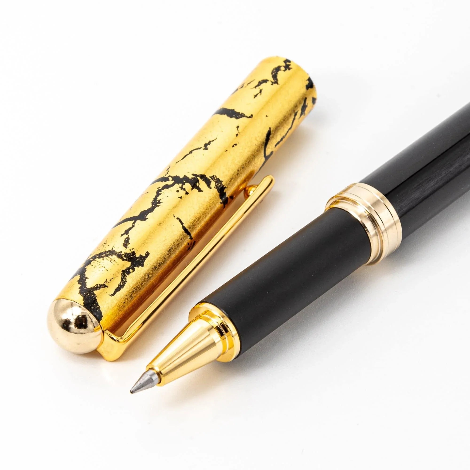 Close-up detail of Japanese black ballpoint pen with gold crackle cap showing fine texture on white background