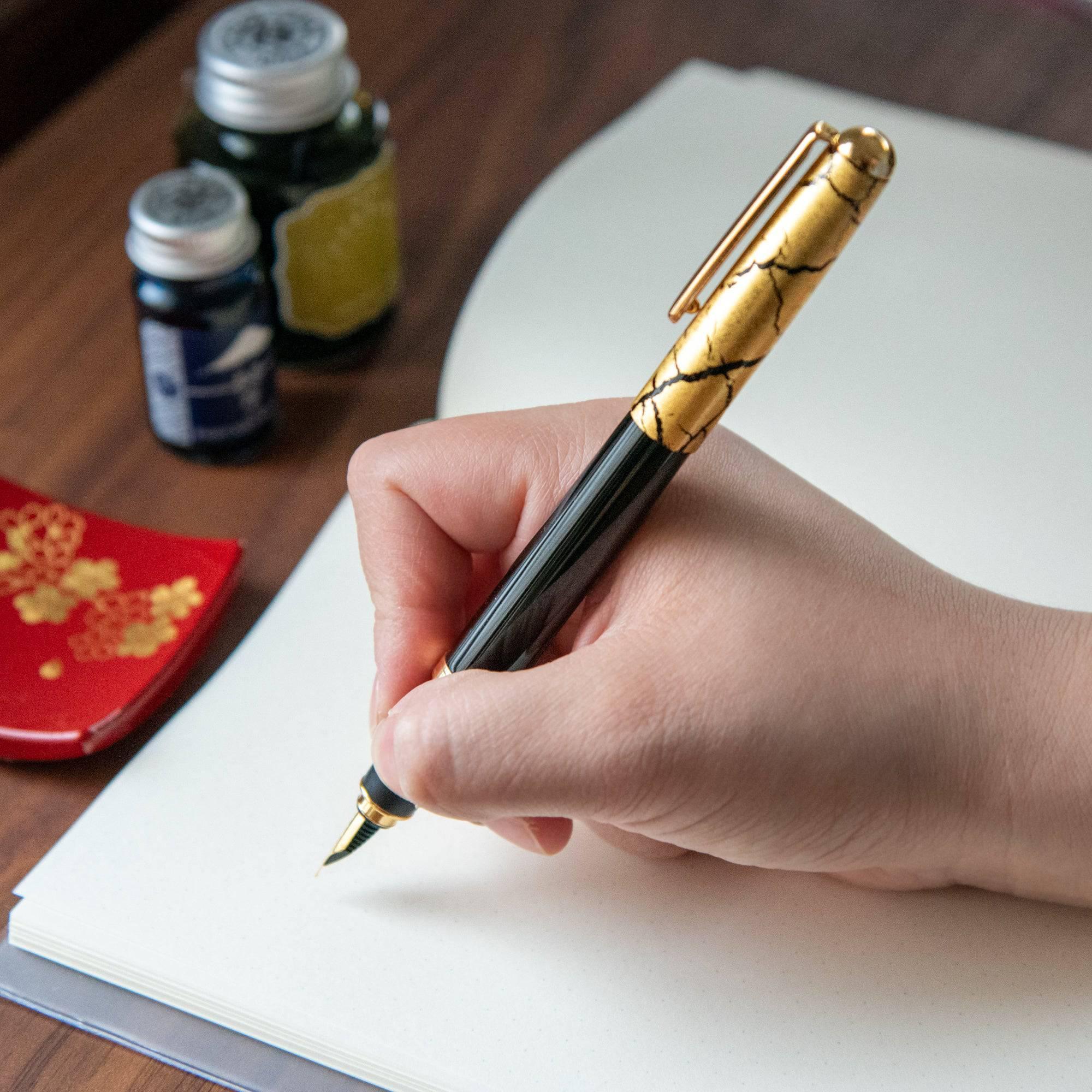 Black fountain pen uncapped, side view showing fine gold leaf texture detail on glossy black lacquer surface