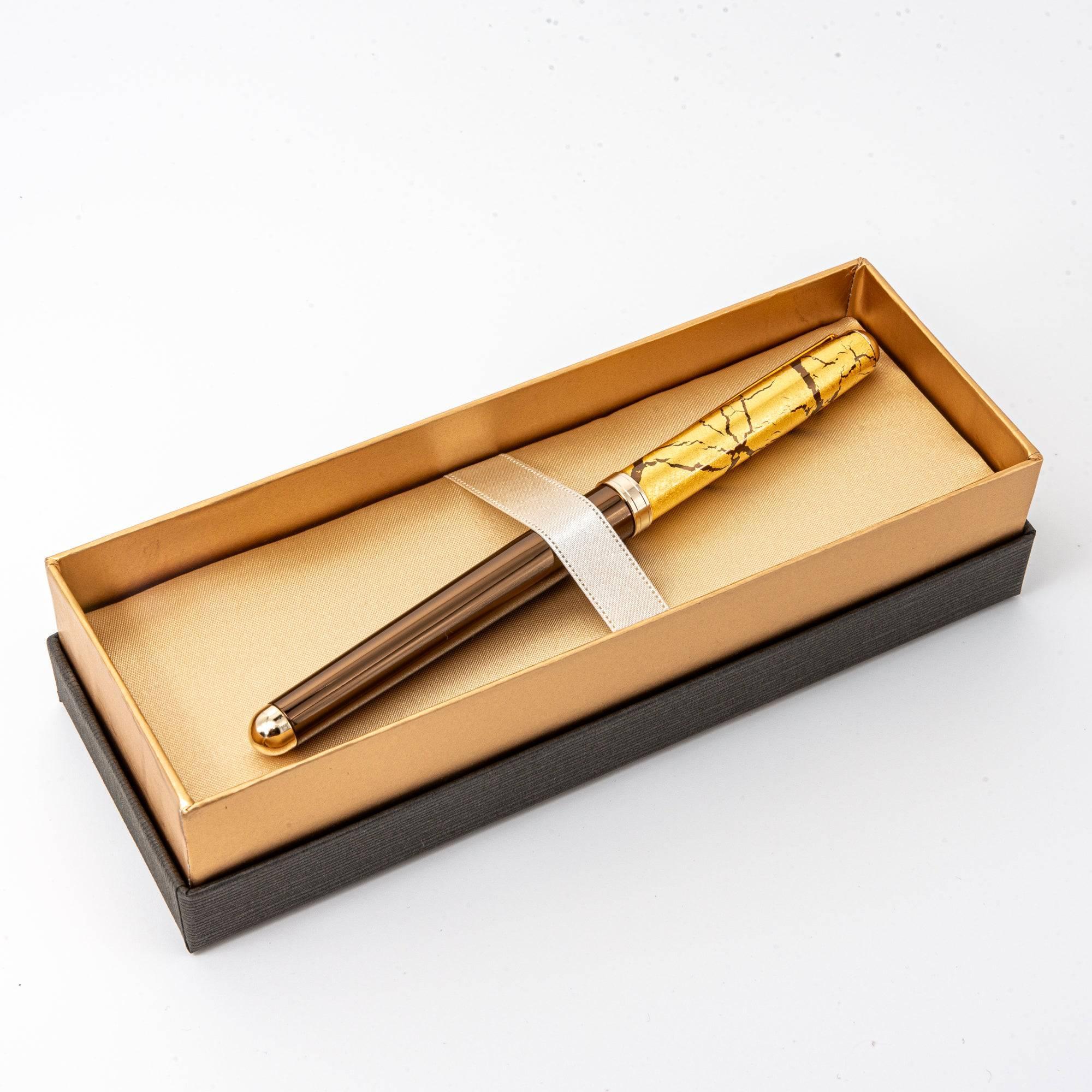Japanese brown ballpoint pen with gold crackle cap held over white paper on wooden desk, in-use shot
