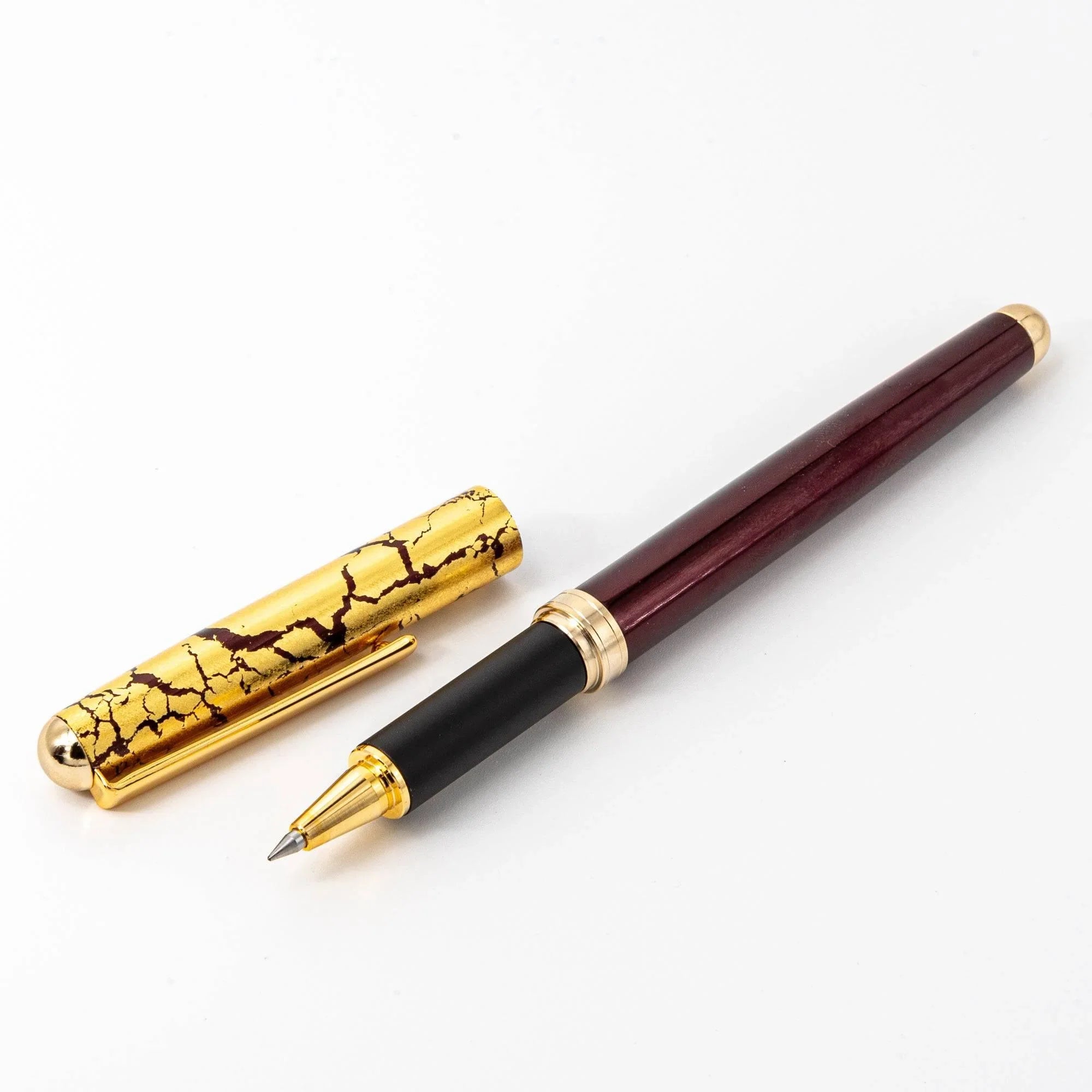 Japanese ballpoint pen wine red lacquer barrel with gold crackle cap and gold bands, capped on white background