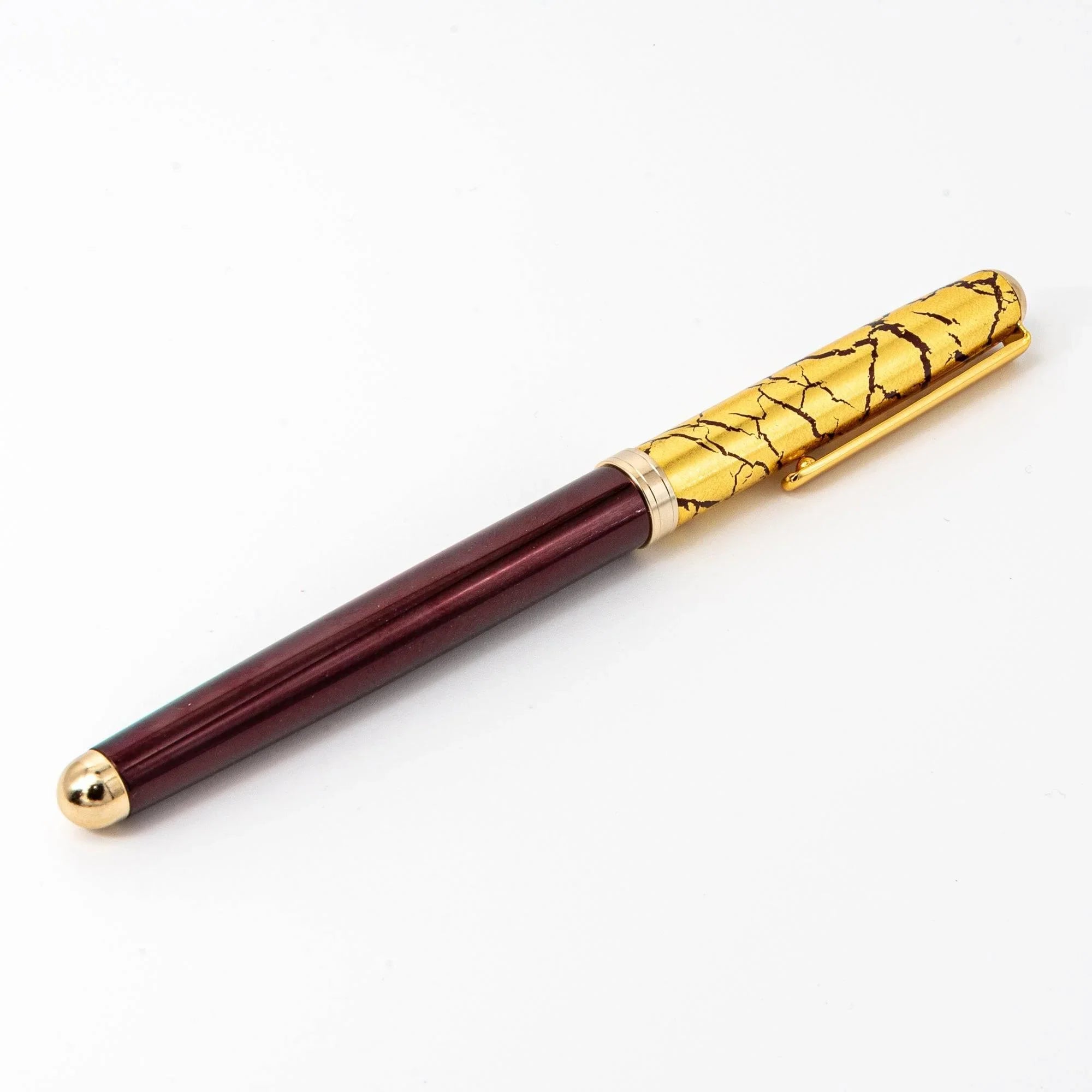 Close-up detail of Japanese gold crackle pattern on wine red ballpoint pen cap, texture focus on white background