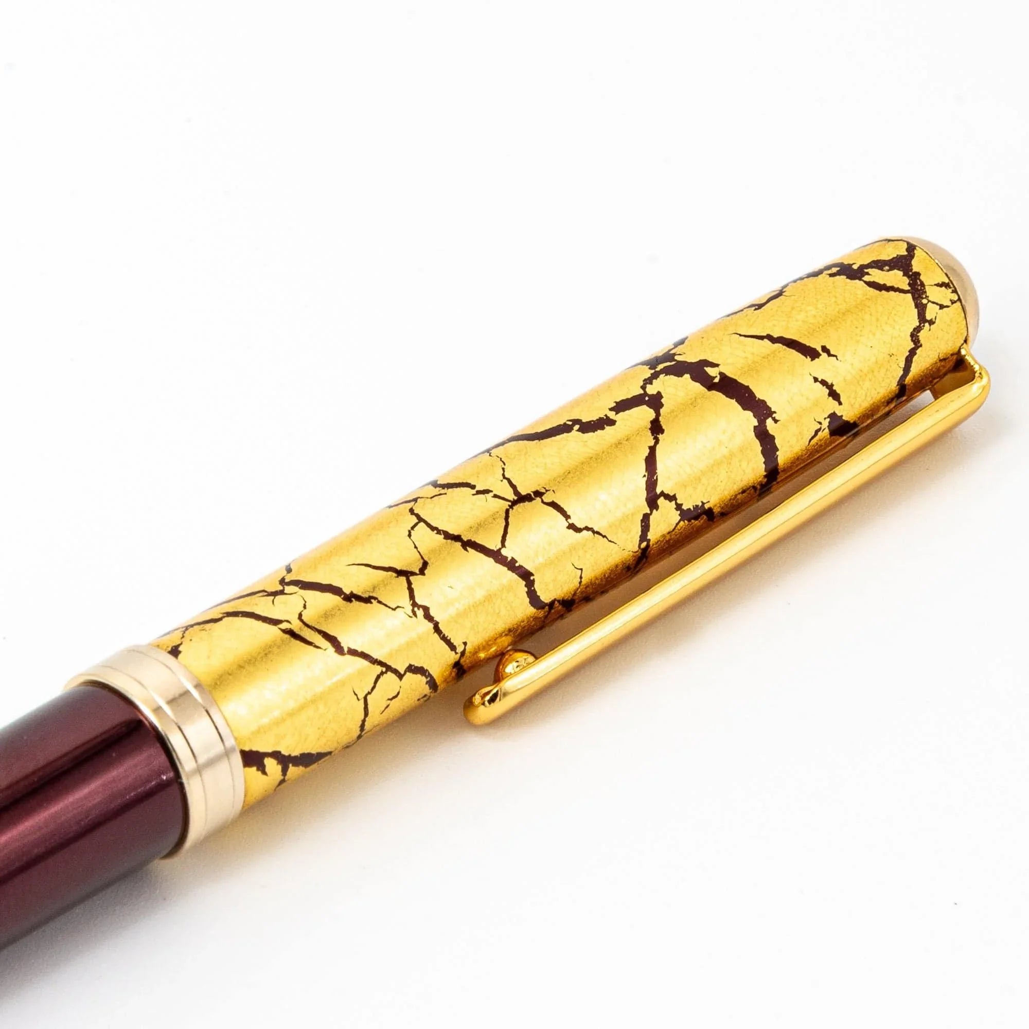 Japanese wine red ballpoint pen capped showing gold crackle cap and gold bands in diagonal view on white