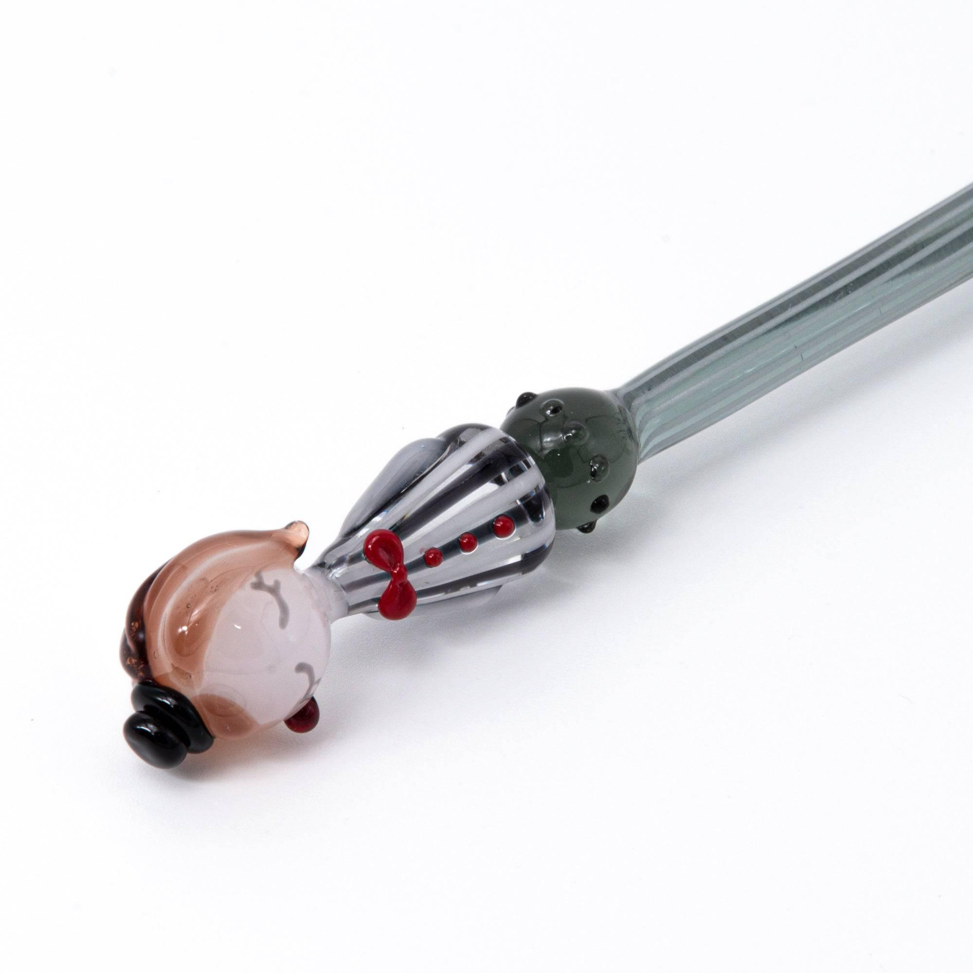 A striped glass dip pen with a whimsical lady figurine top, featuring elegant curves and handcrafted details.