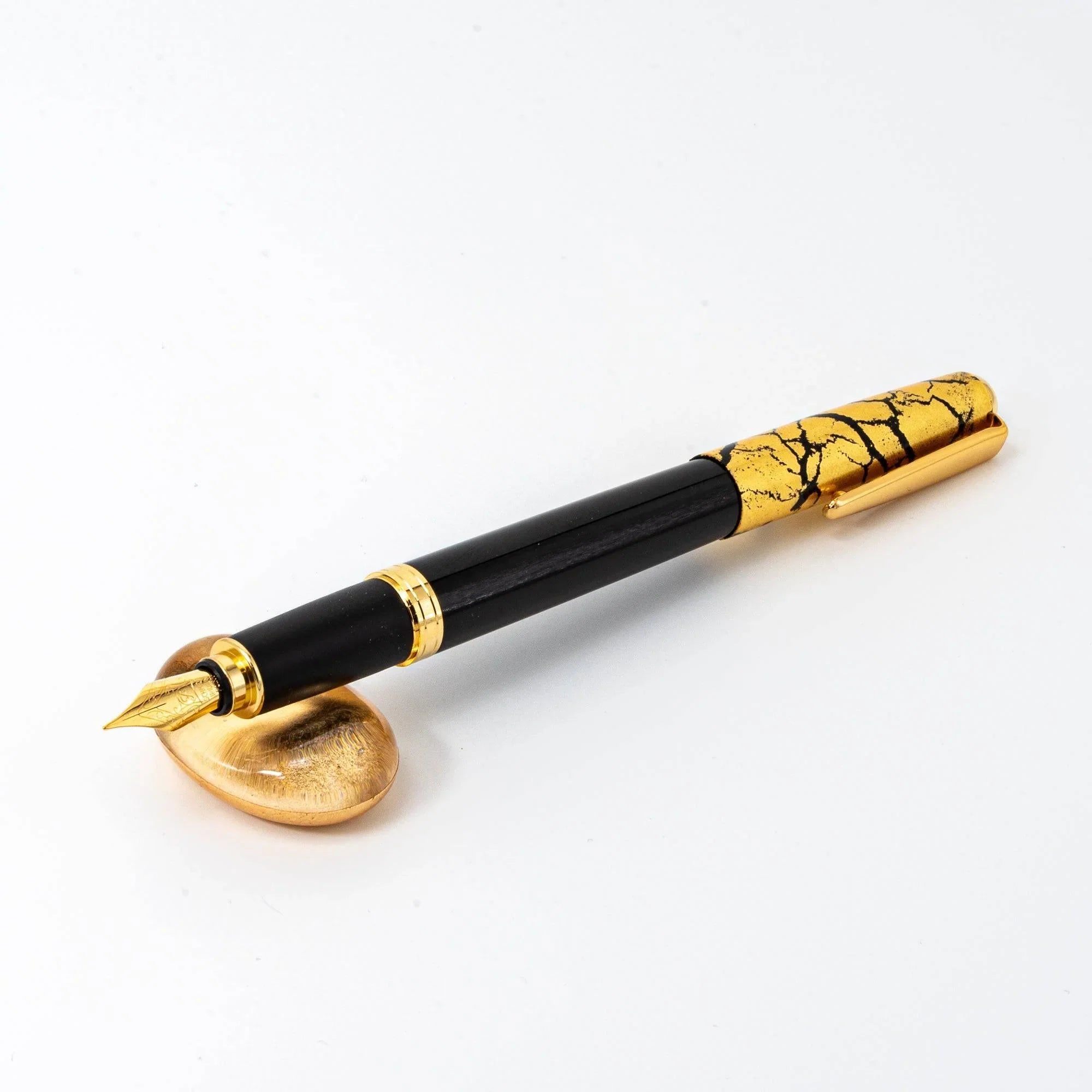 Japanese gold-toned glass pen rest with floating gold leaf accents displayed beside black lacquered dip pen composition