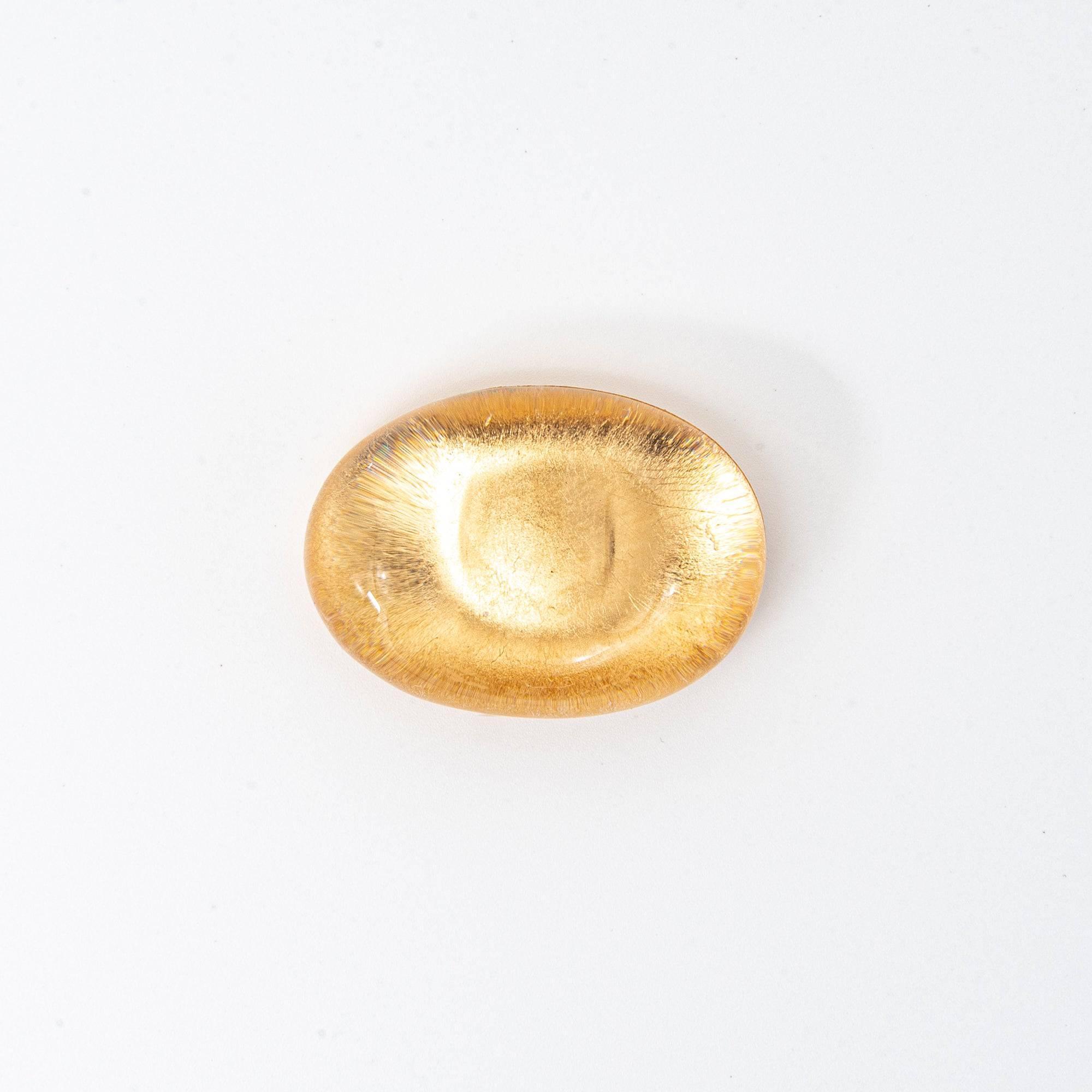 A smooth oval glass pen rest with gold-leaf interior reflecting a luminous sheen, showcasing an elegant and minimalist design, perfect for desk use.