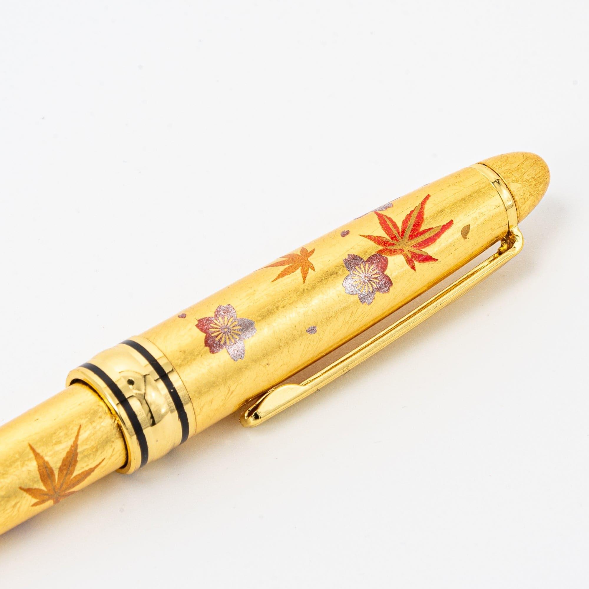 A golden pen with delicate sakura and momiji leaf patterns, showcasing its detailed lacquer finish and elegant clip design.