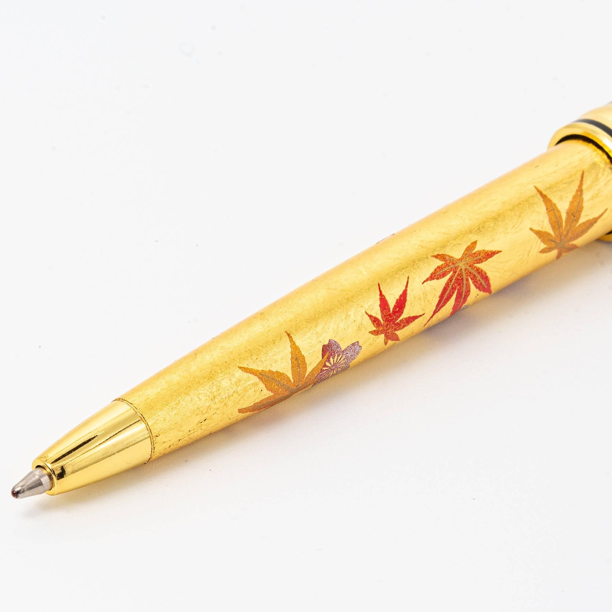 A detailed view of the gold pen’s lower barrel, adorned with vibrant red maple leaves and cherry blossoms on a shimmering background.