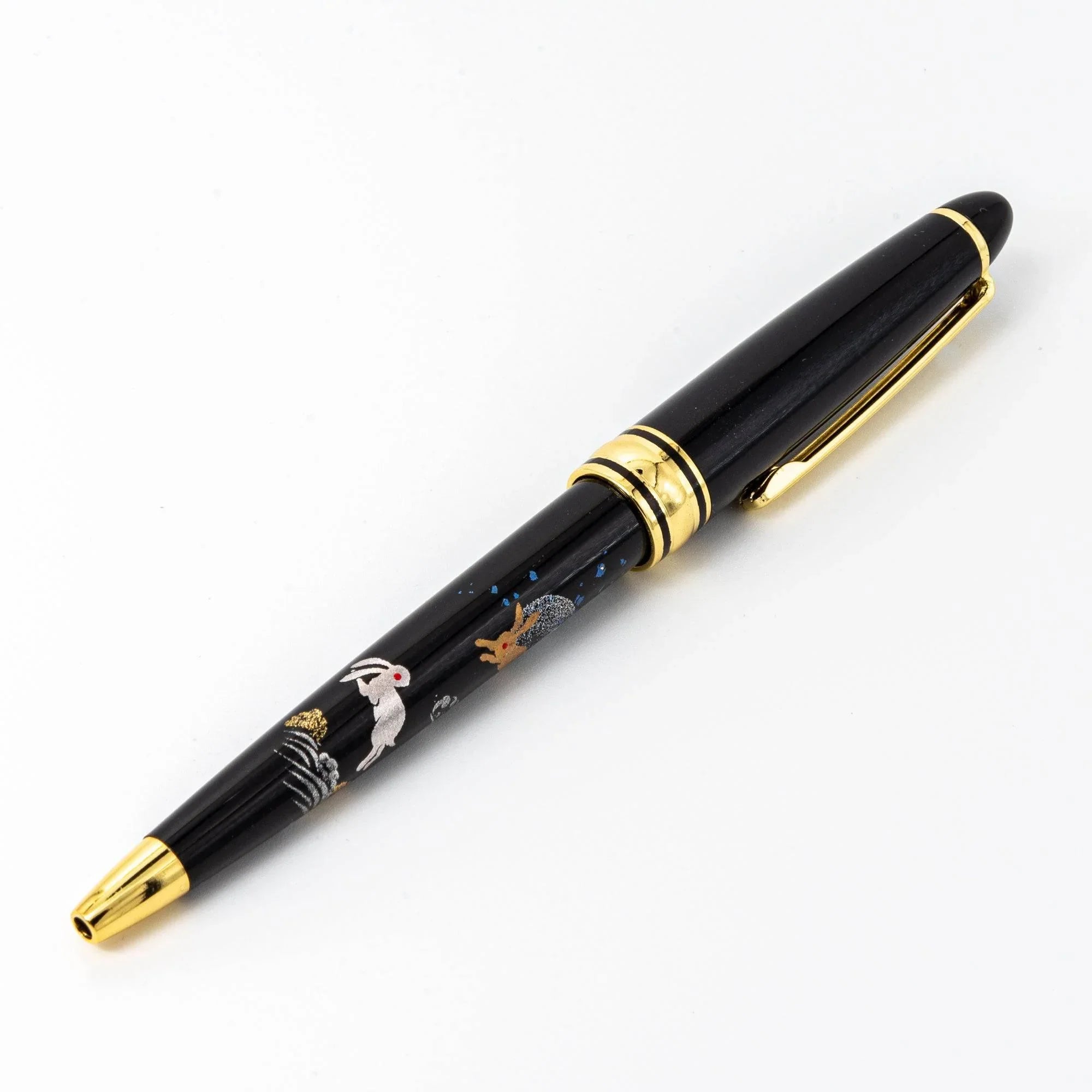 Capped black ballpoint pen with gold rabbit and moon makie art, gold bands, white background with clear visibility of design