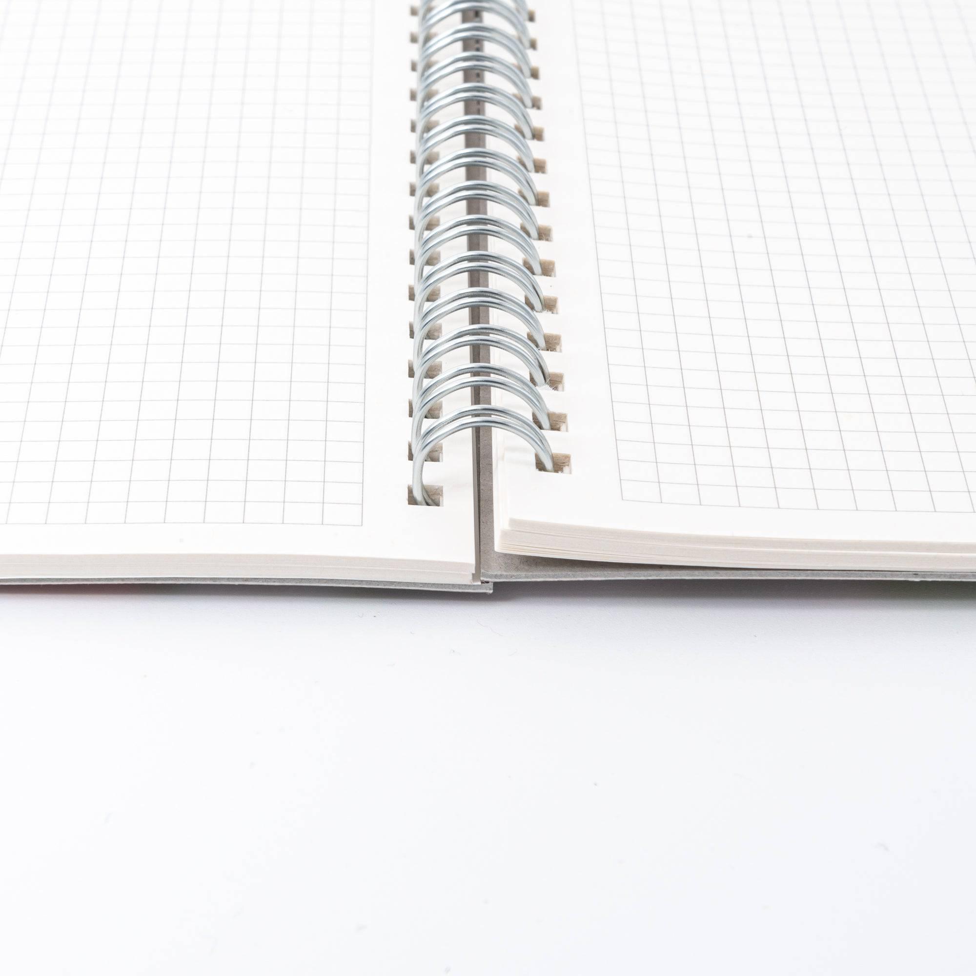 Open spiral-bound Japanese notebook with grid paper and a plain cardboard back cover, emphasizing functionality and simplicity in design.