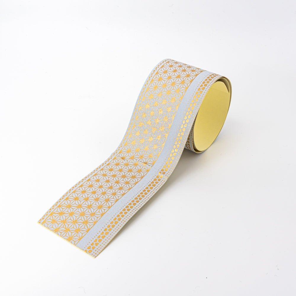 Golden yuzen washi tape unrolled diagonally showing asanoha and kikko border patterns in gold on grey, yellow backing visible