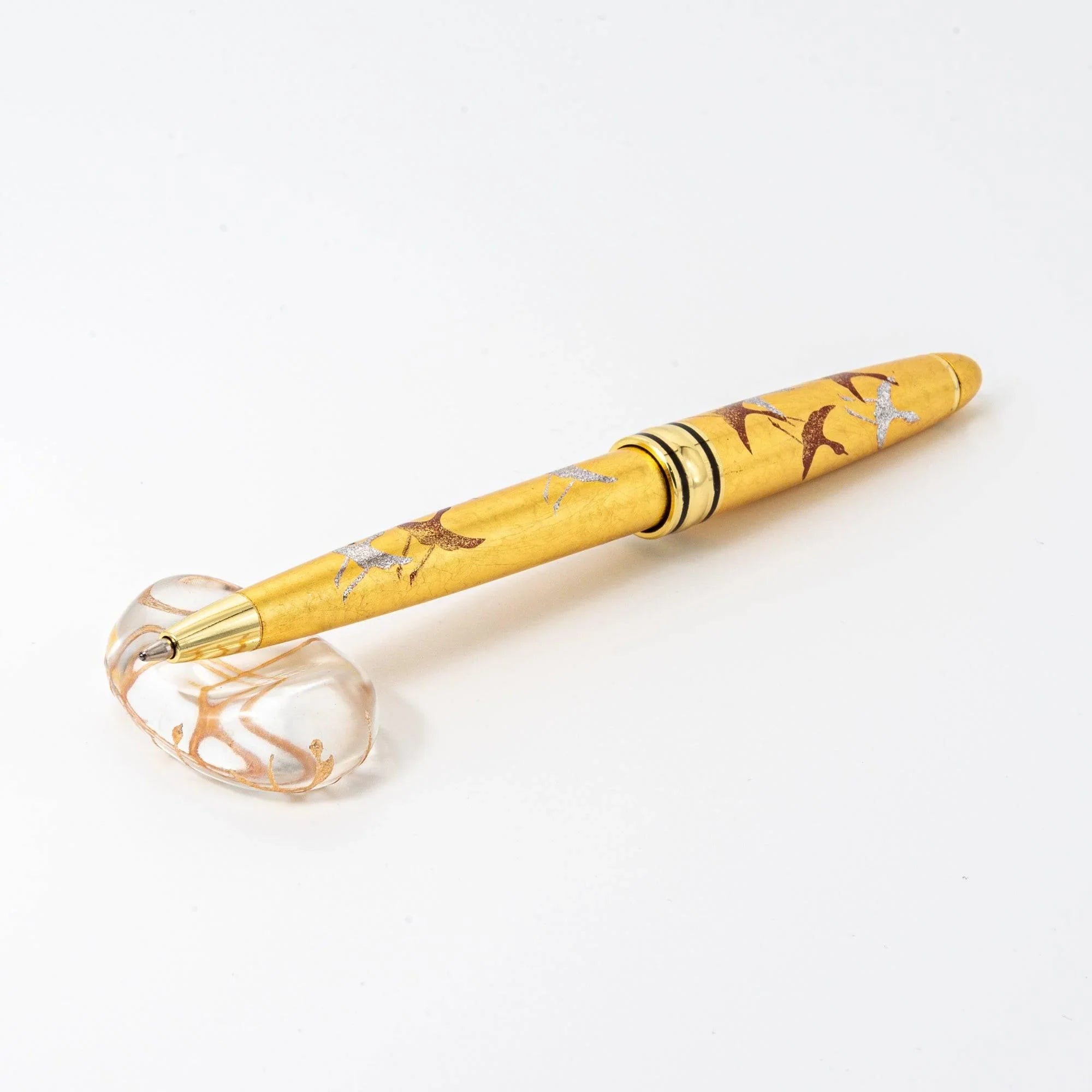Clear glass oval pen rest with gold thread interior design displayed beside wooden ballpoint pen, side profile