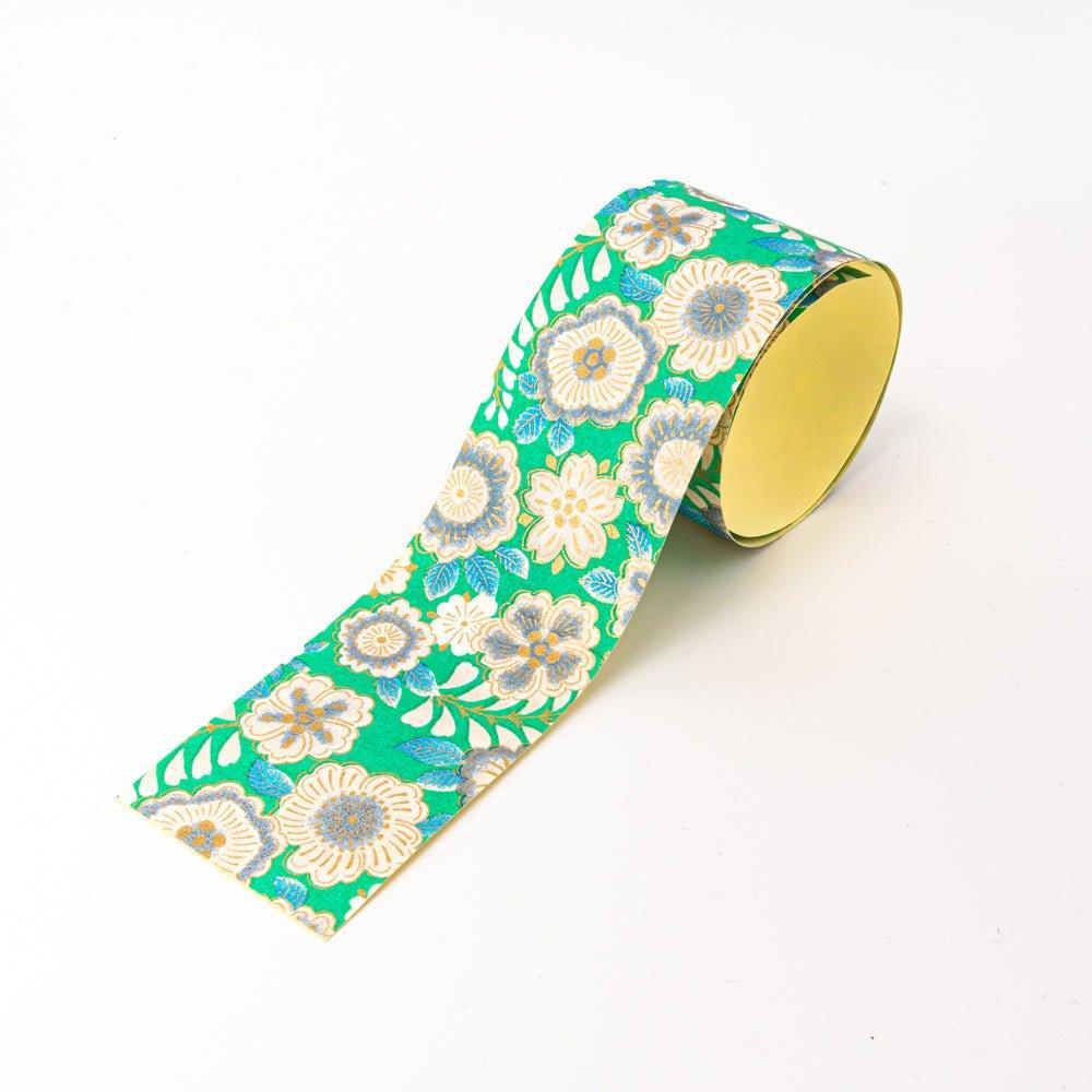 Roll of Japanese yuzen washi tape partially unrolled, bright green with cream garden flowers, blue leaves, and gold accents
