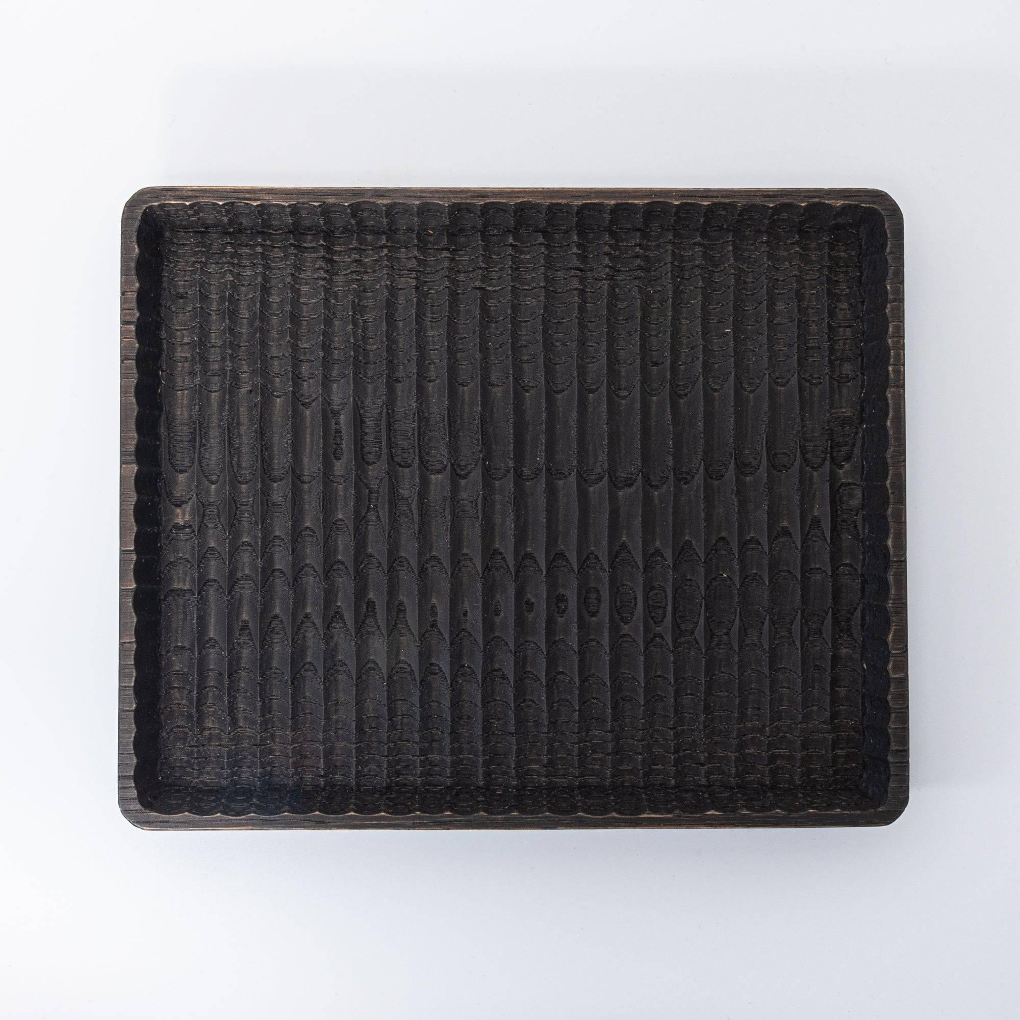 Black wooden tray with intricate carved grooves and a smooth raised edge, displayed flat on a white surface.