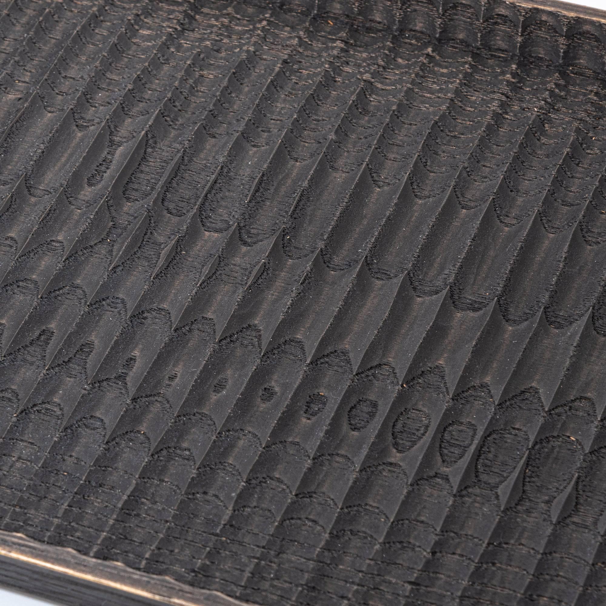 Angled view of a black wooden tray showing its intricate carved patterns and smooth finish.