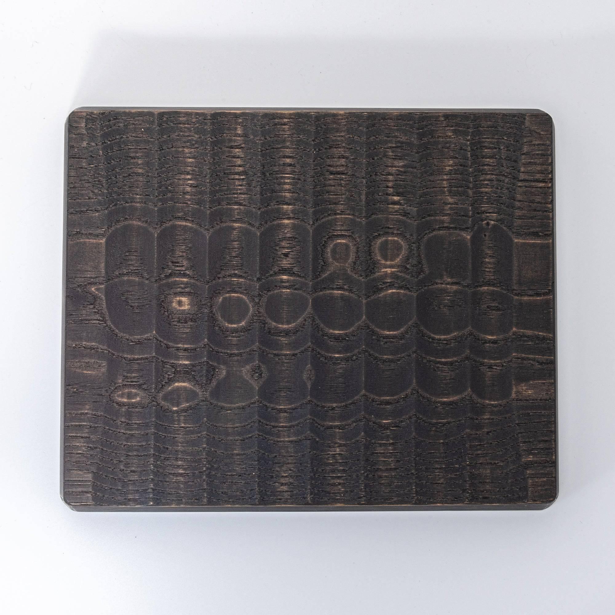 Flat black wooden board with intricate carved patterns, showcasing a textured surface.