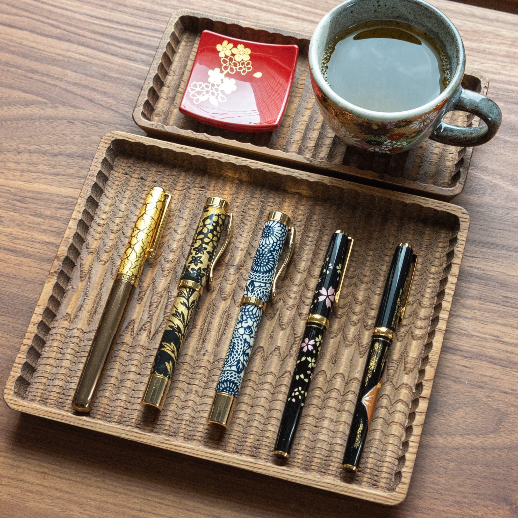 Light wood pen tray with carved wave-pattern channels, five slots with pens, natural wood grain with clear visibility of