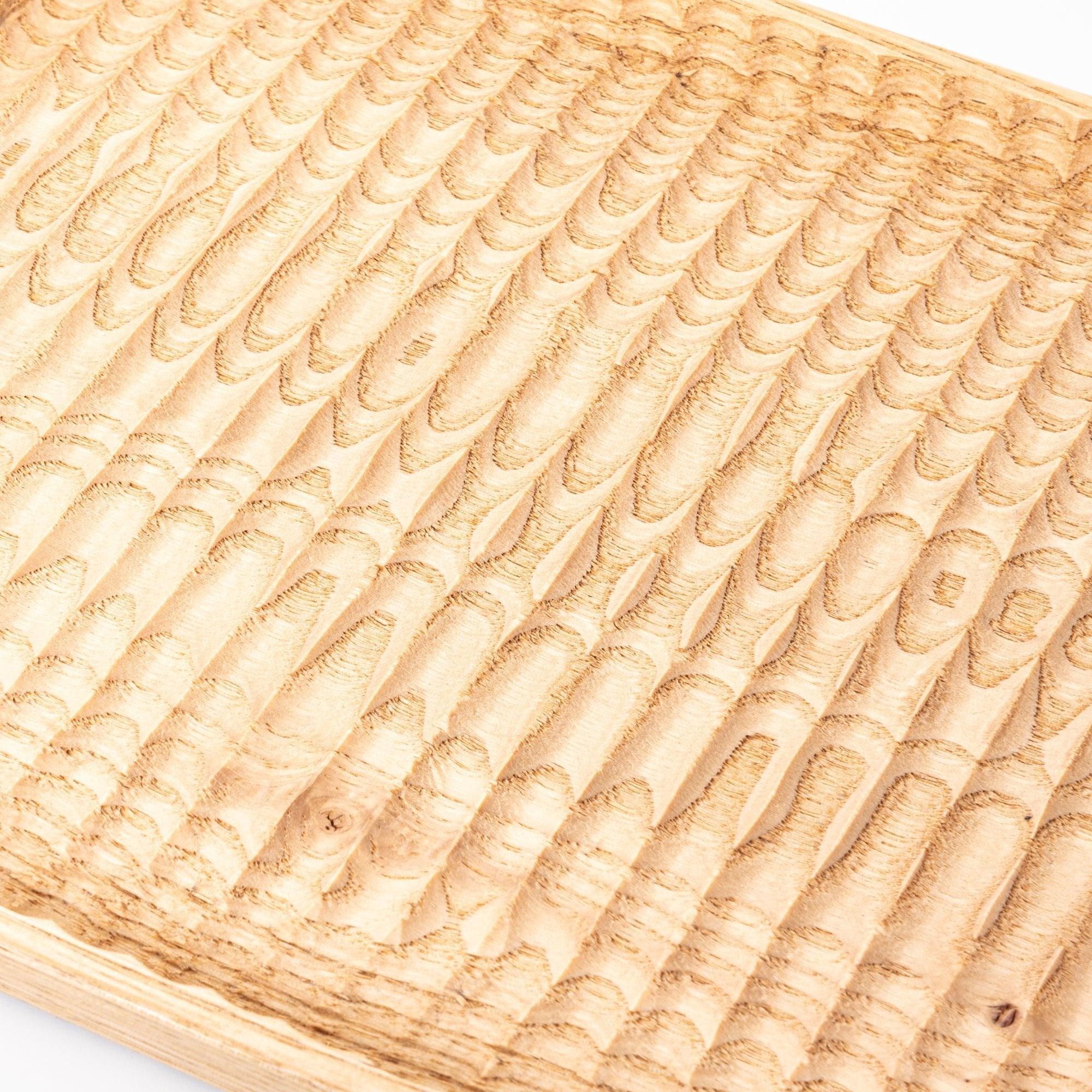 Angled view of a wooden tray emphasizing its carved grooves and smooth edges, placed on a white surface.
