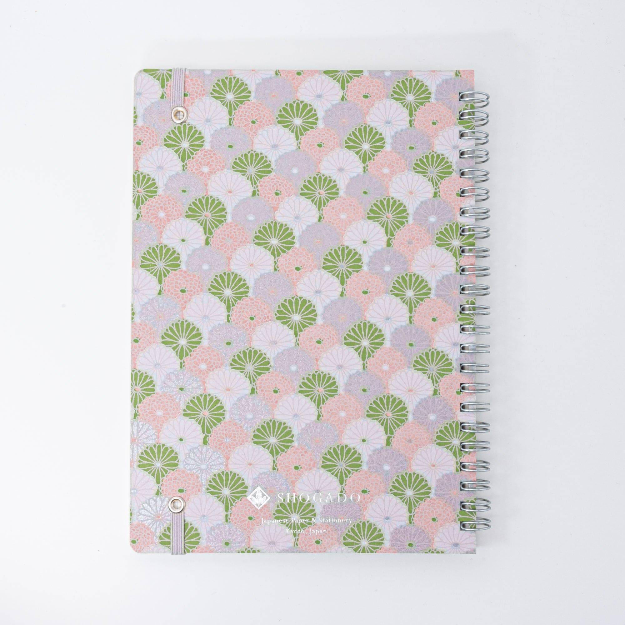 A Japanese notebook with a Yuzen washi cover, showcasing a pastel fan pattern in green, pink, and lilac, with a silver spiral binding and elastic band.