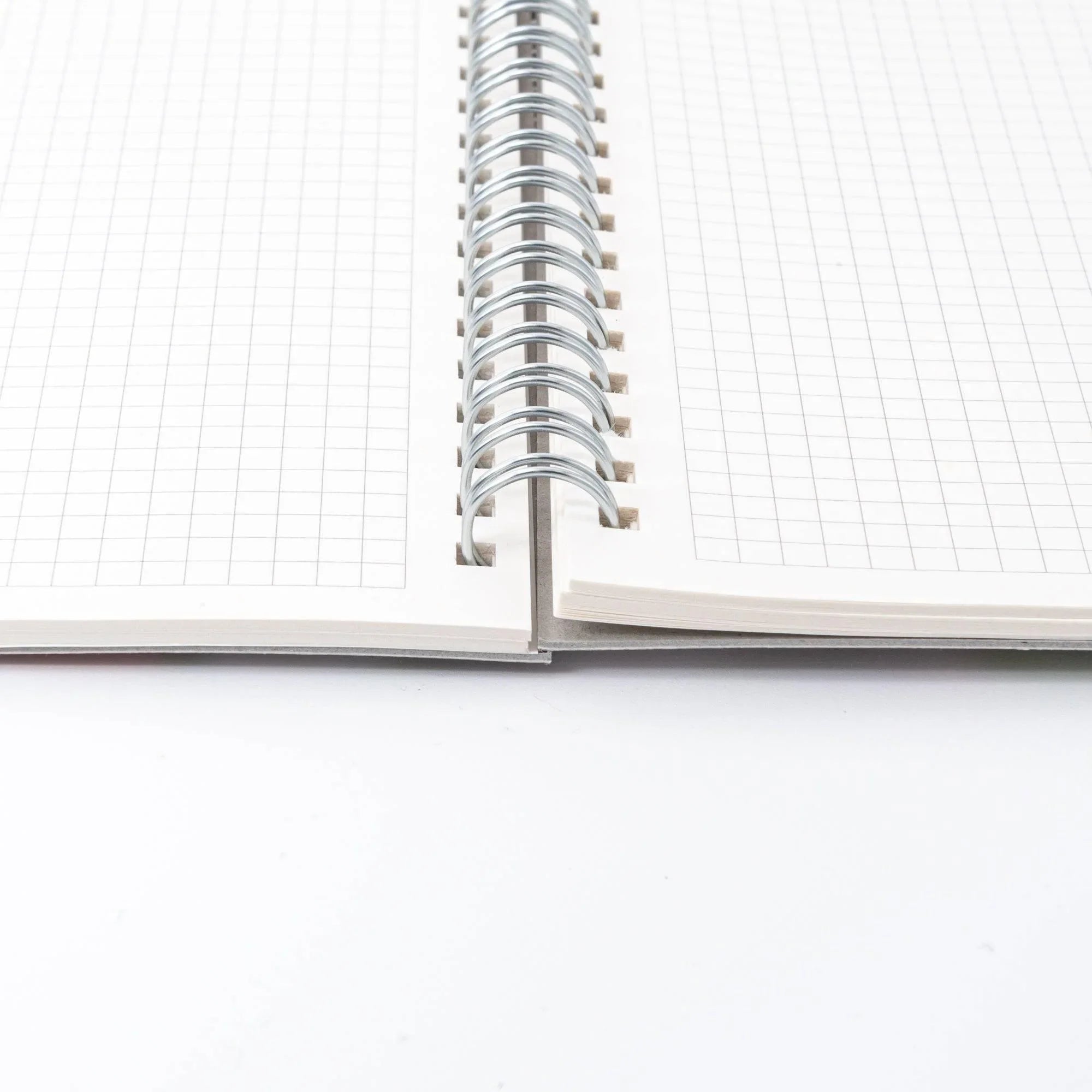 Japanese yuzen washi notebook open from a low angle showing silver spiral binding and fine grid pages on both sides