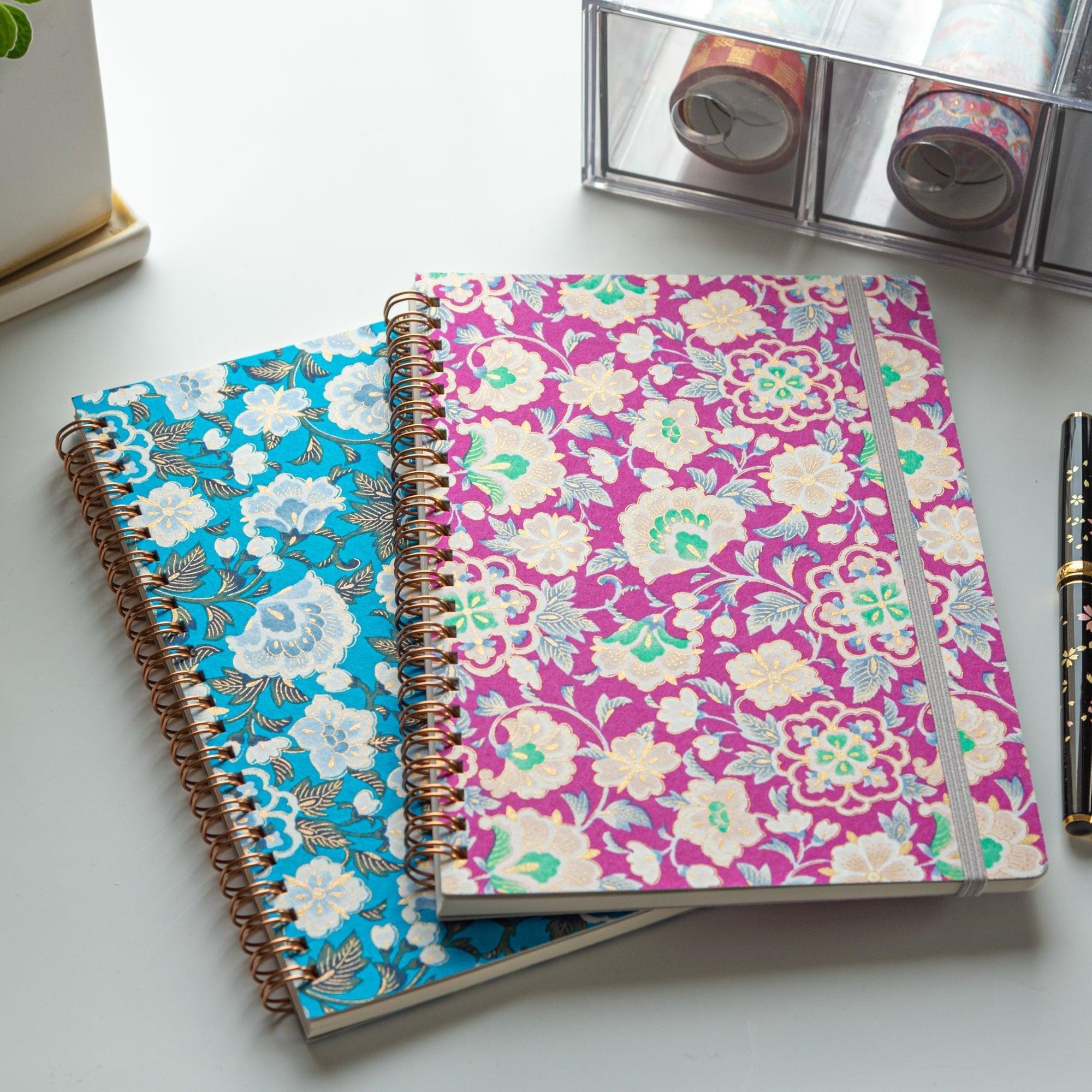 Two Japanese notebooks with Yuzen washi covers. One features a pink floral design, the other blue, both with rose gold spiral bindings.
