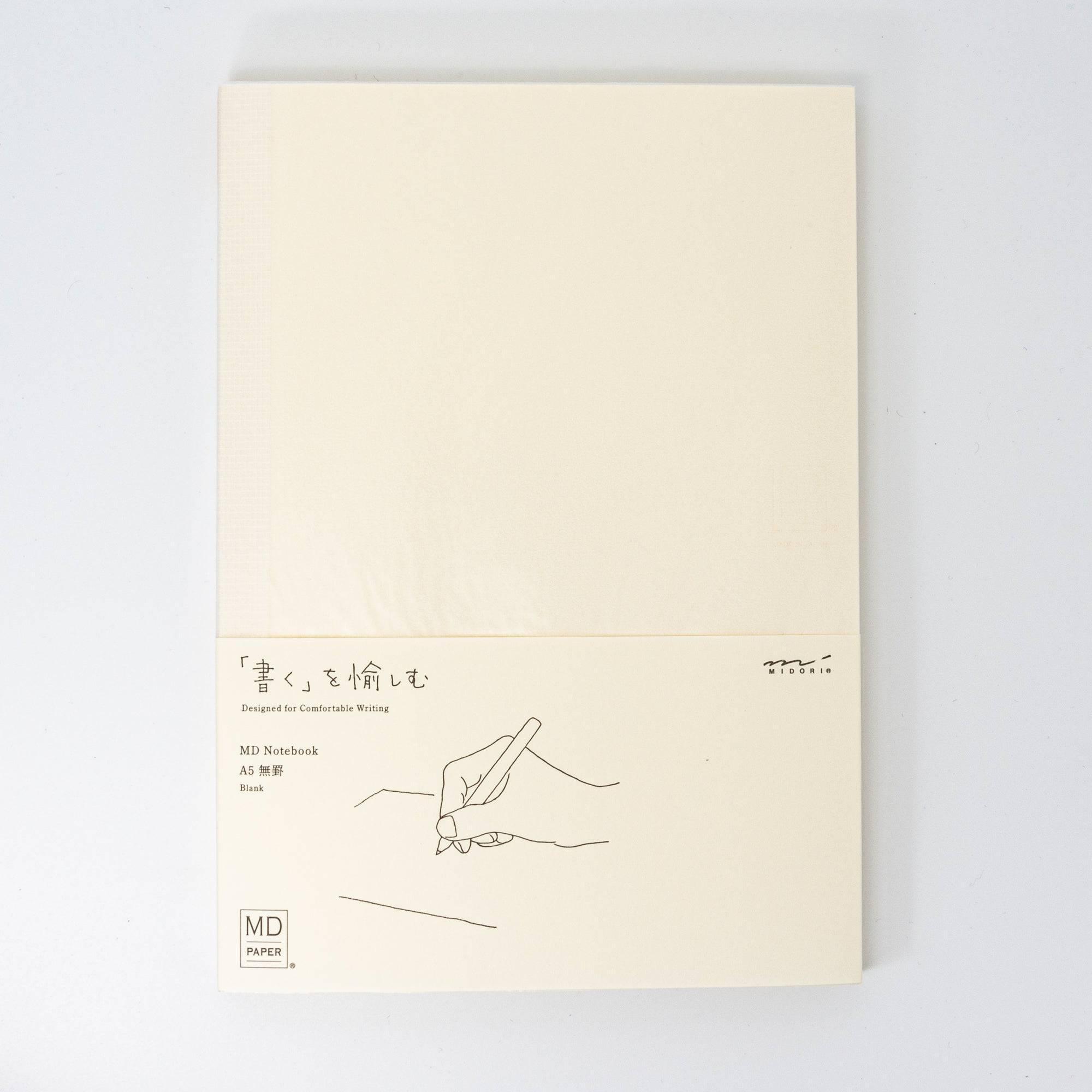 A Japanese stationery MD Notebook with a blank layout, featuring a simple beige cover and a white band with an illustration of writing.
