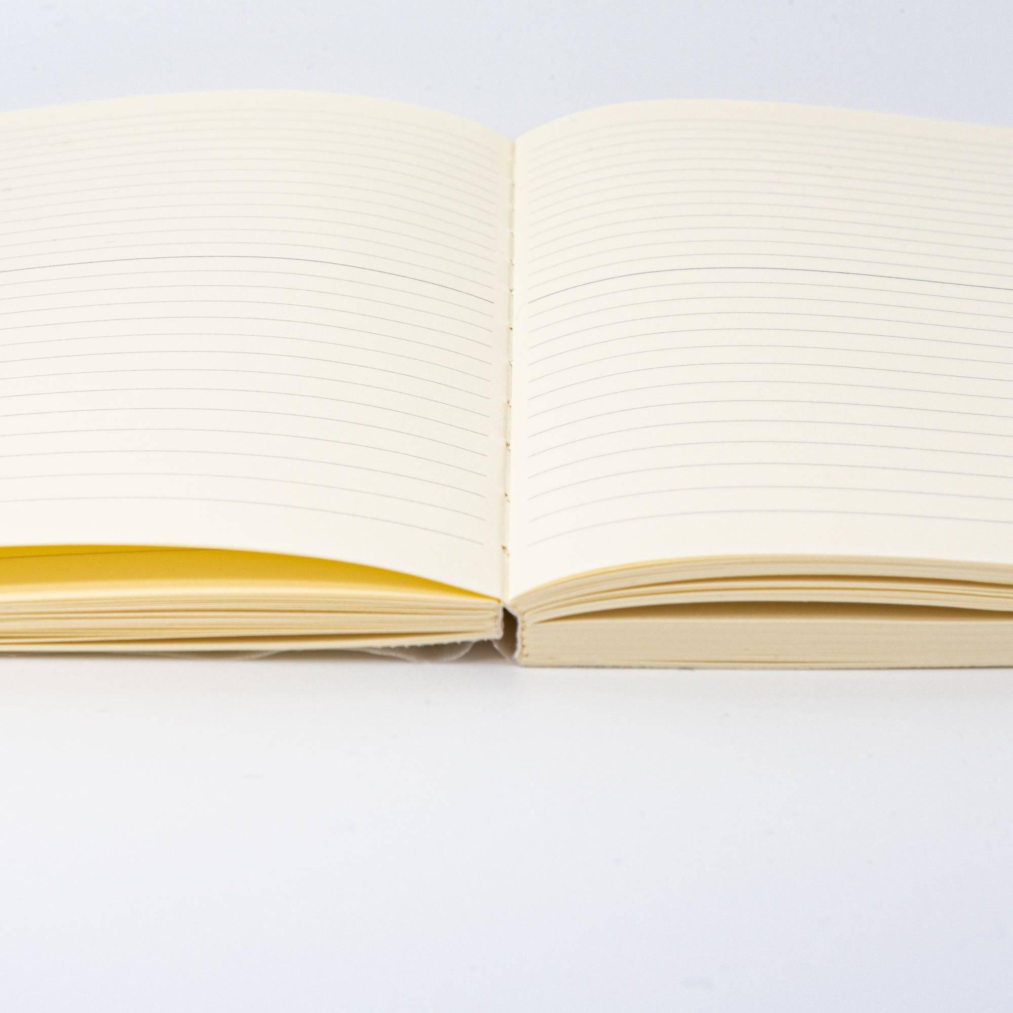 An open Japanese stationery MD Notebook showing its stitched binding and cream-colored lined pages, designed for durability and smooth writing.