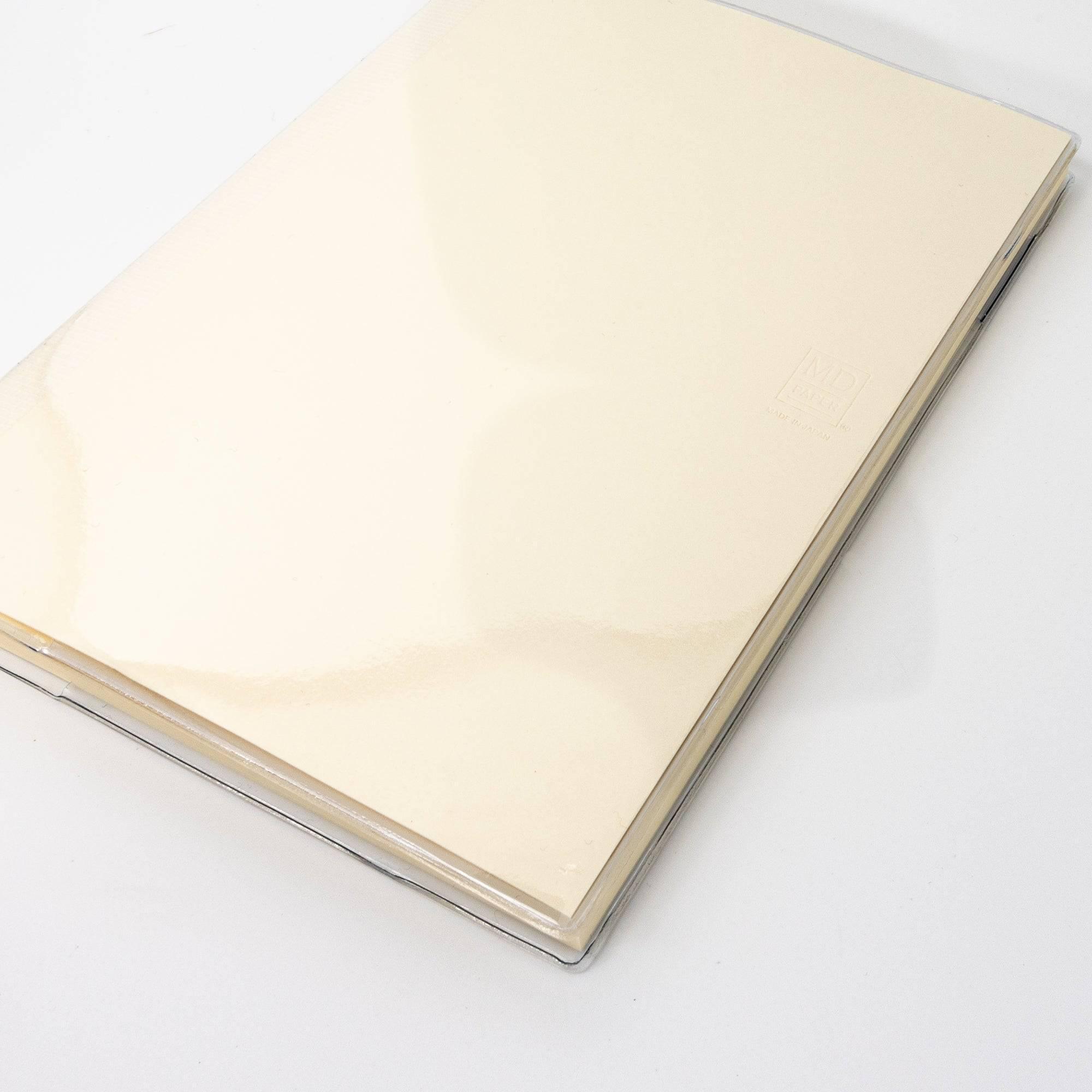 An MD notebook with a transparent cover, showing its cream-colored pages, included as part of Japanese stationery.
