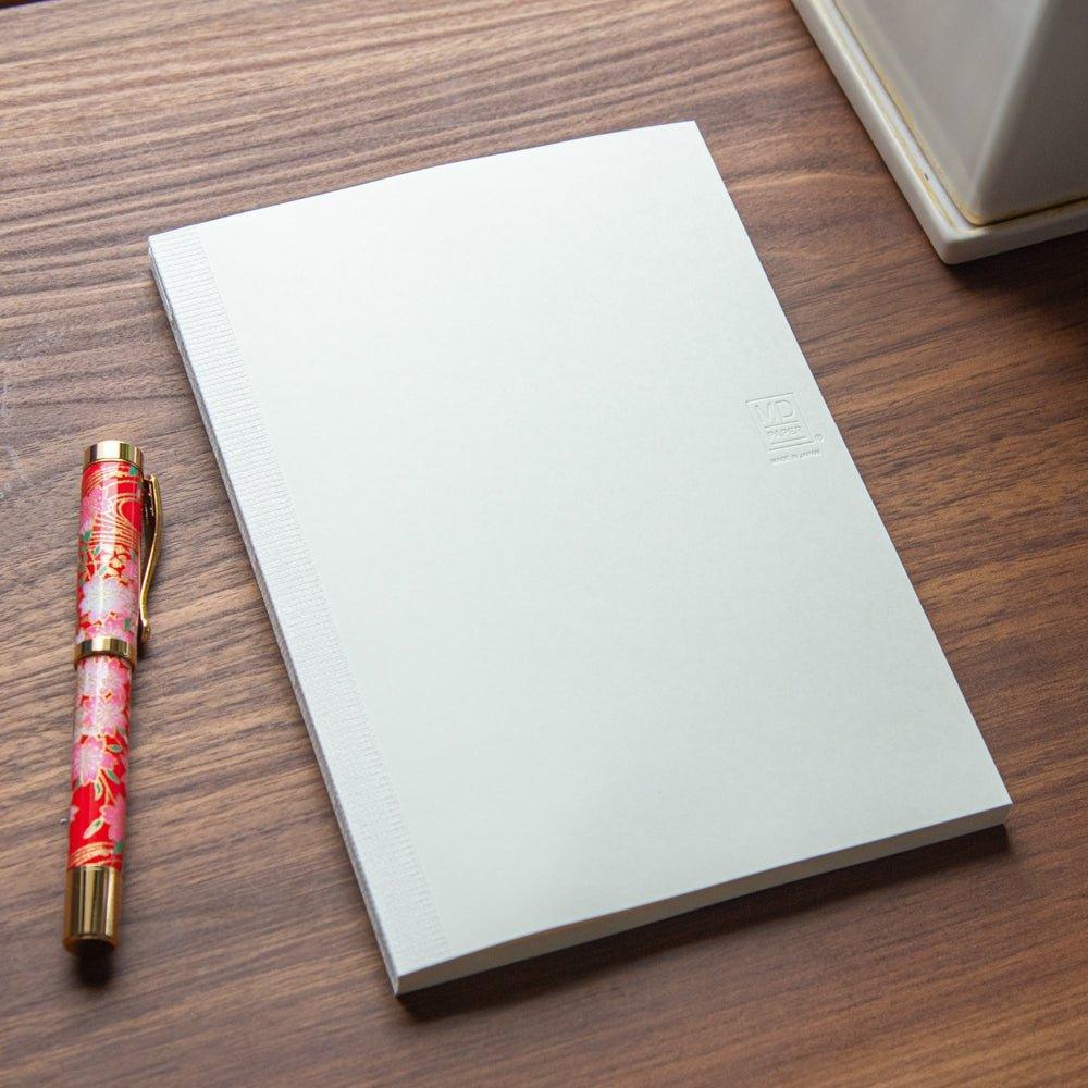 The back of an MD notebook with a textured spine, paired with a red floral fountain pen, showcasing Japanese stationery.