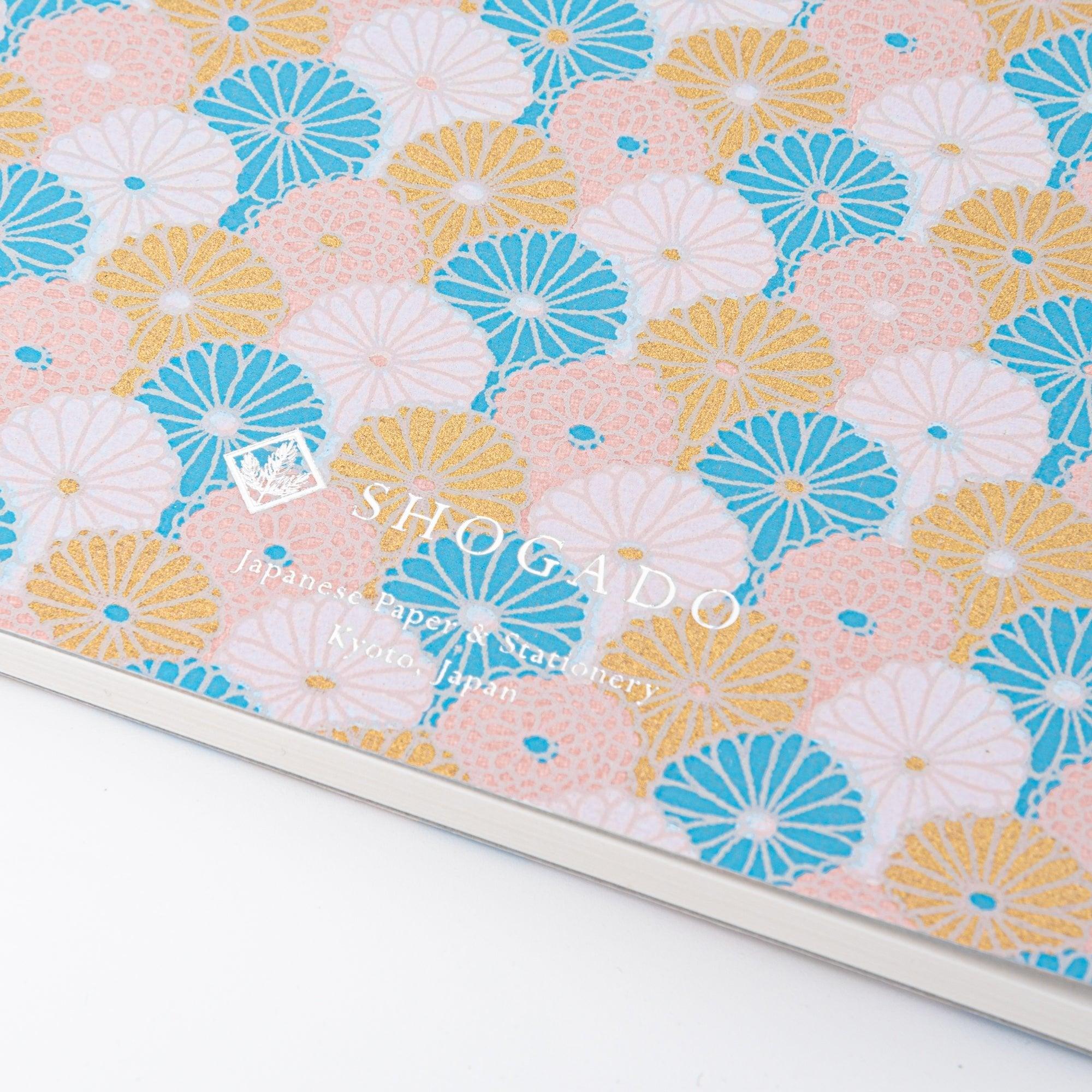 Spiral-bound Japanese notebook with a hand-dyed Yuzen washi cover, featuring fan-shaped patterns in blue, gold, and pink, showcasing Japanese stationery craftsmanship.