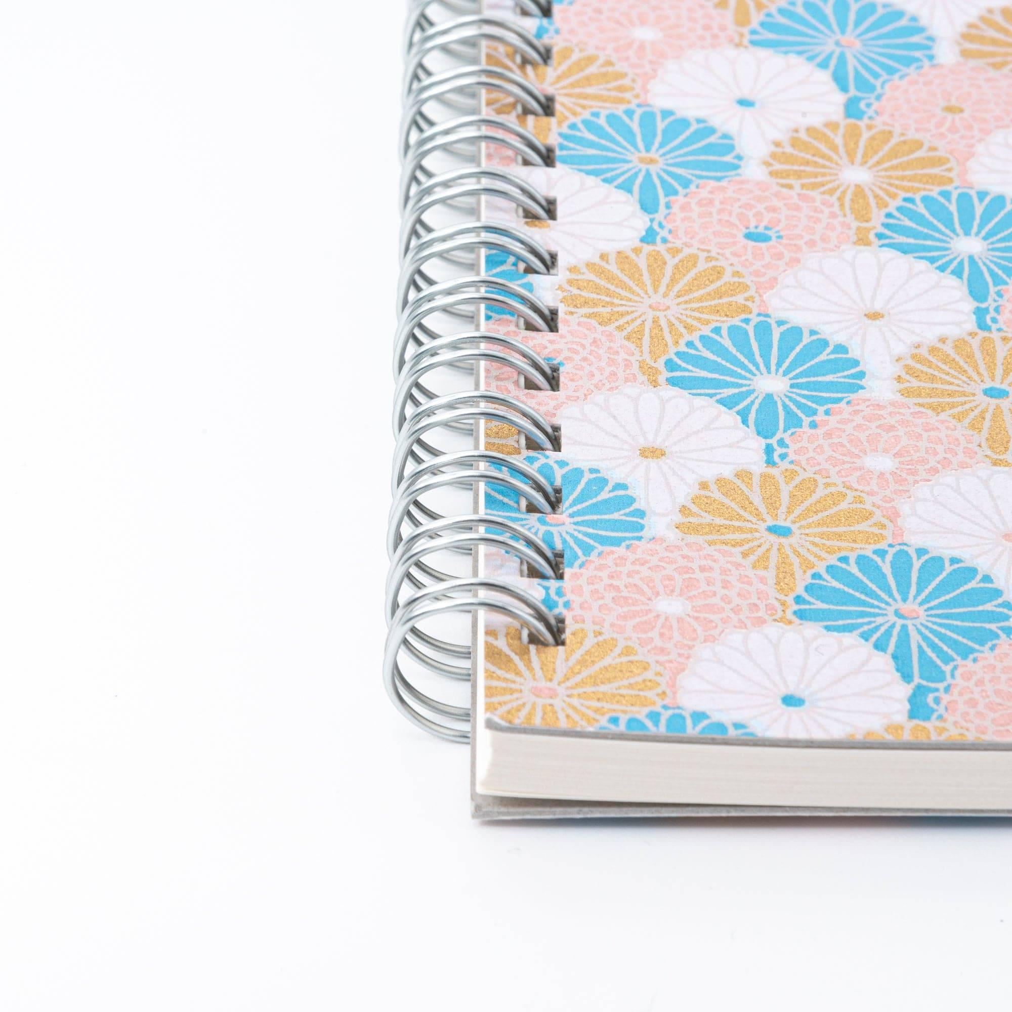 Spiral-bound Japanese notebook with a hand-dyed Yuzen washi cover, featuring fan-shaped patterns in blue, gold, and pink, showcasing Japanese stationery craftsmanship.