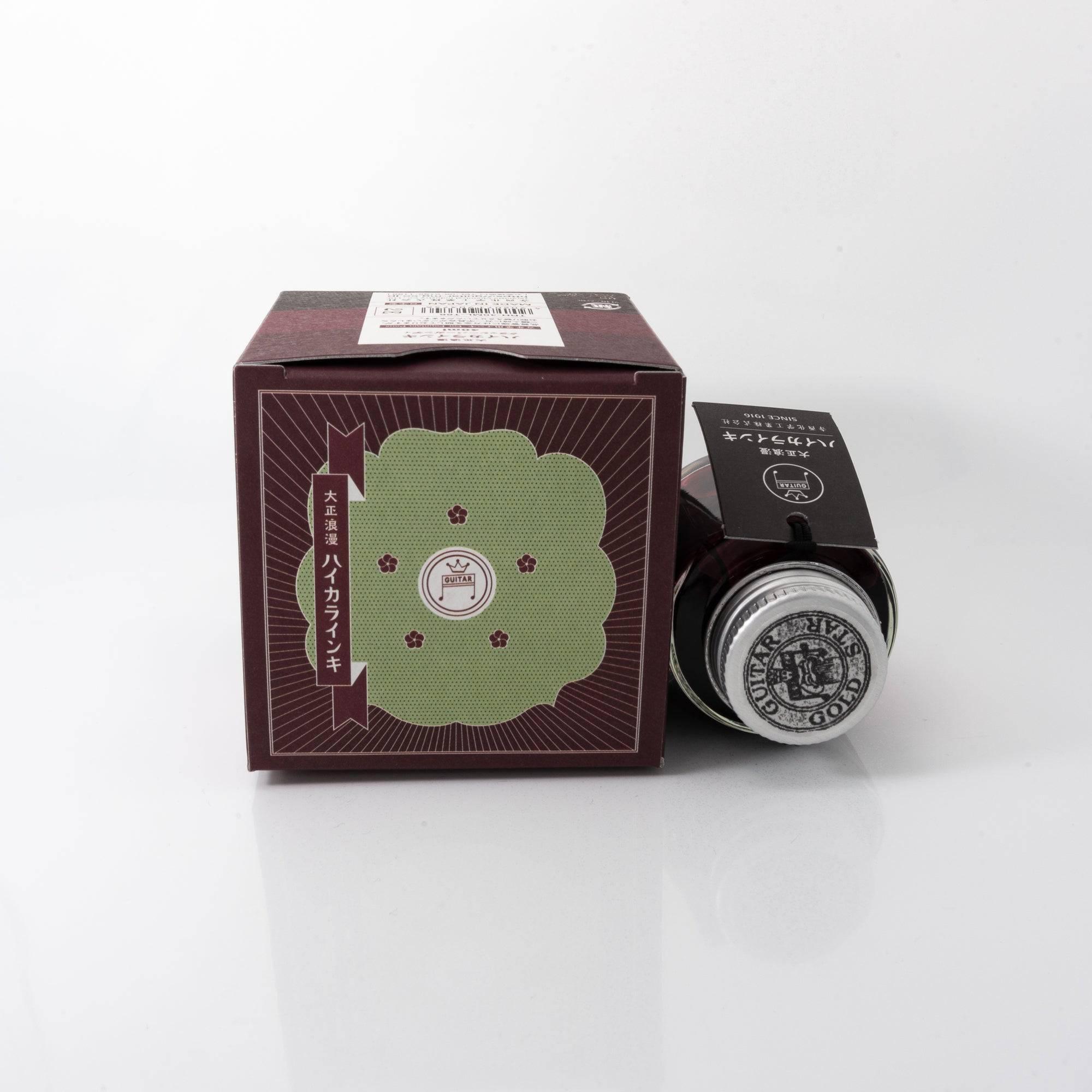 Taisho Romance Classy Burgundy fountain pen ink bottle and matching pen, arranged on a wooden desk, emphasizing a classic design.