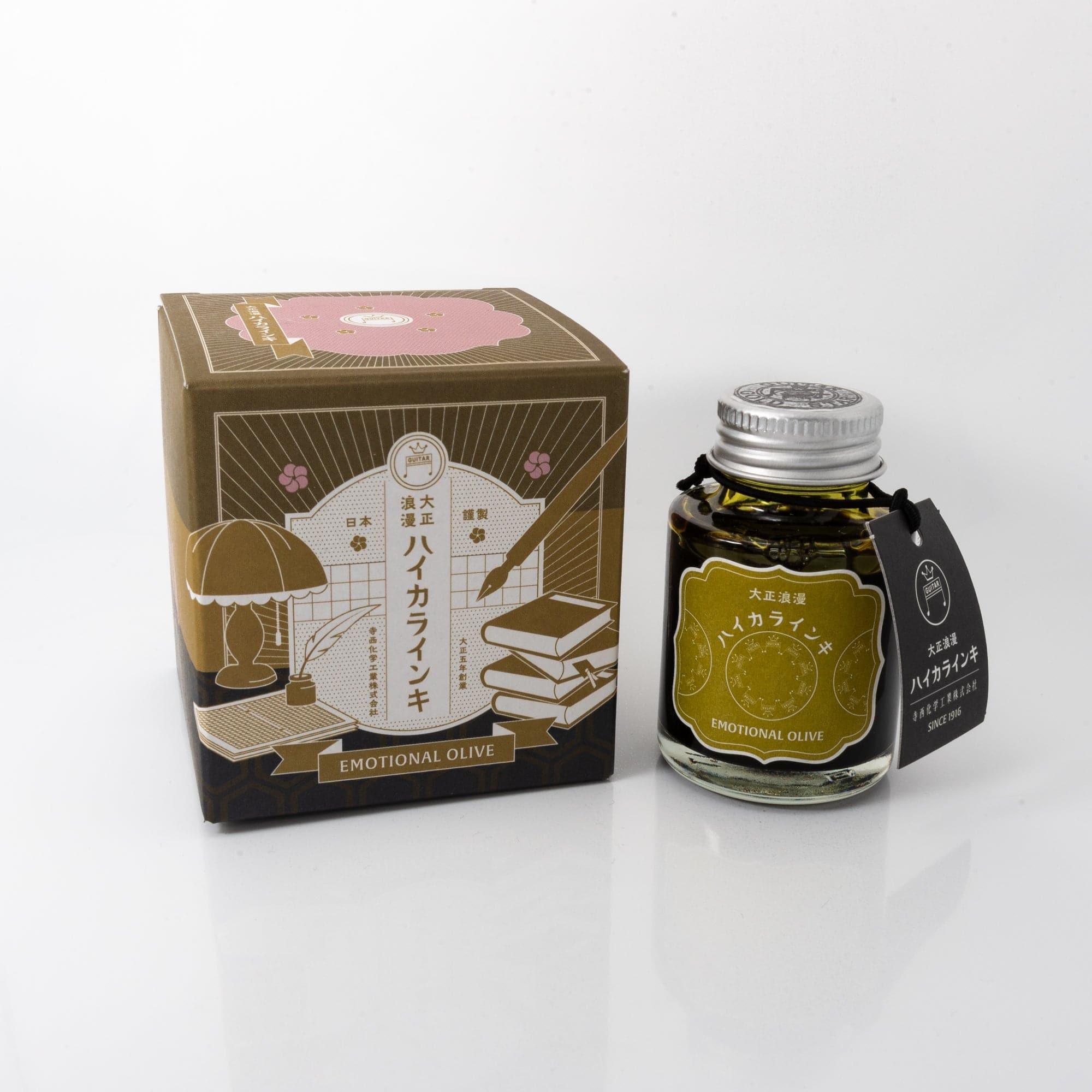 Taisho Romance Emotional Olive fountain pen ink bottle with a muted olive hue, placed on a wooden desk under soft natural light.