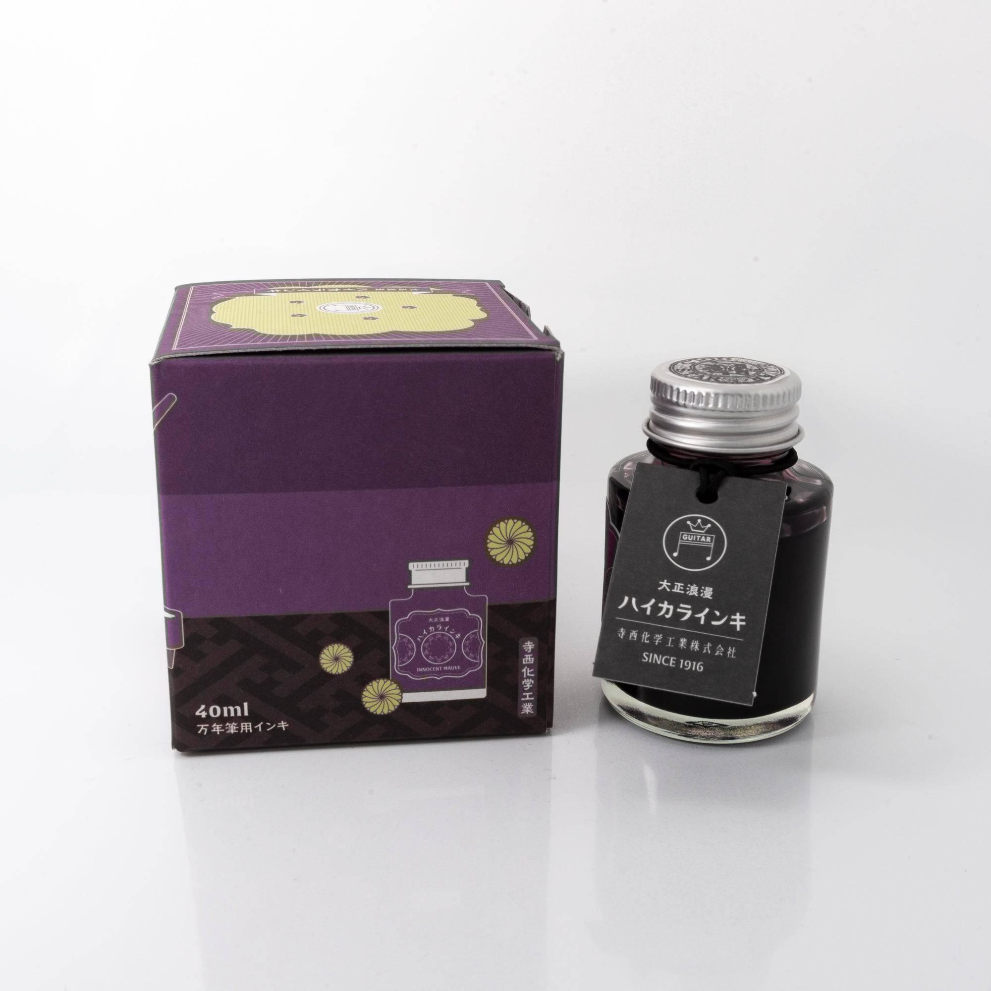 Open Taisho Romance Innocent Mauve ink bottle with subtle mauve liquid, placed beside a fountain pen, blending elegance and functionality.