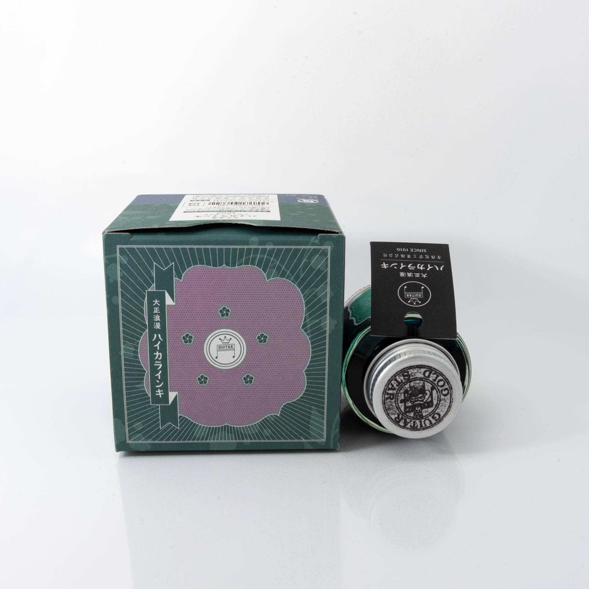 Taisho Romance Lady Emerald fountain pen ink bottle and matching pen, arranged on a wooden desk, emphasizing a timeless design.